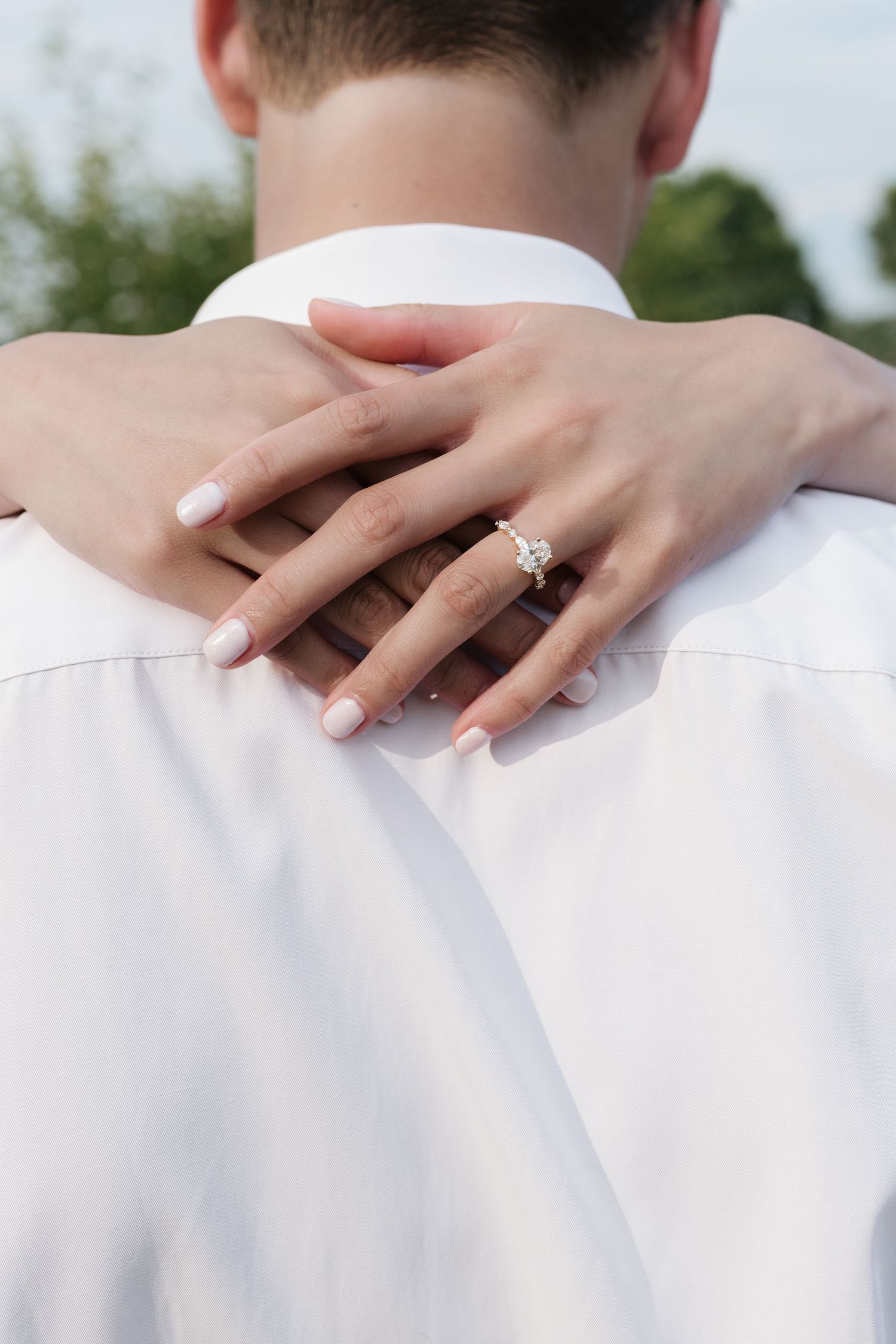 Close-up of a woman's hand with a diamond engagement ring resting on her partner's white shirt.