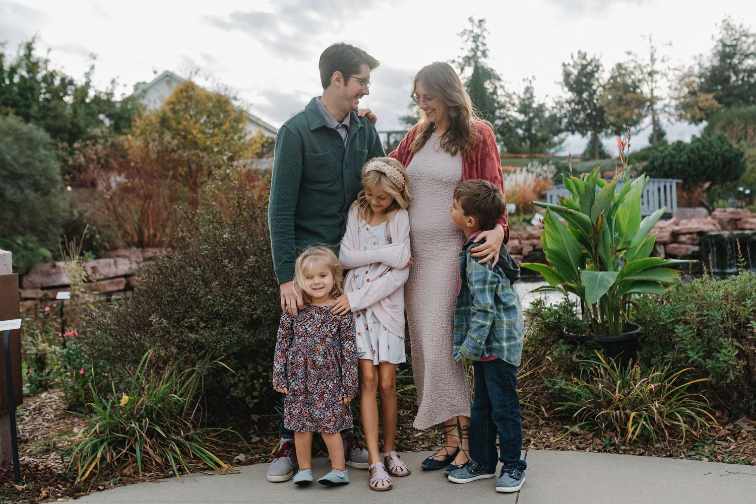 Loving family of five sharing a warm embrace in a lush autumn garden.