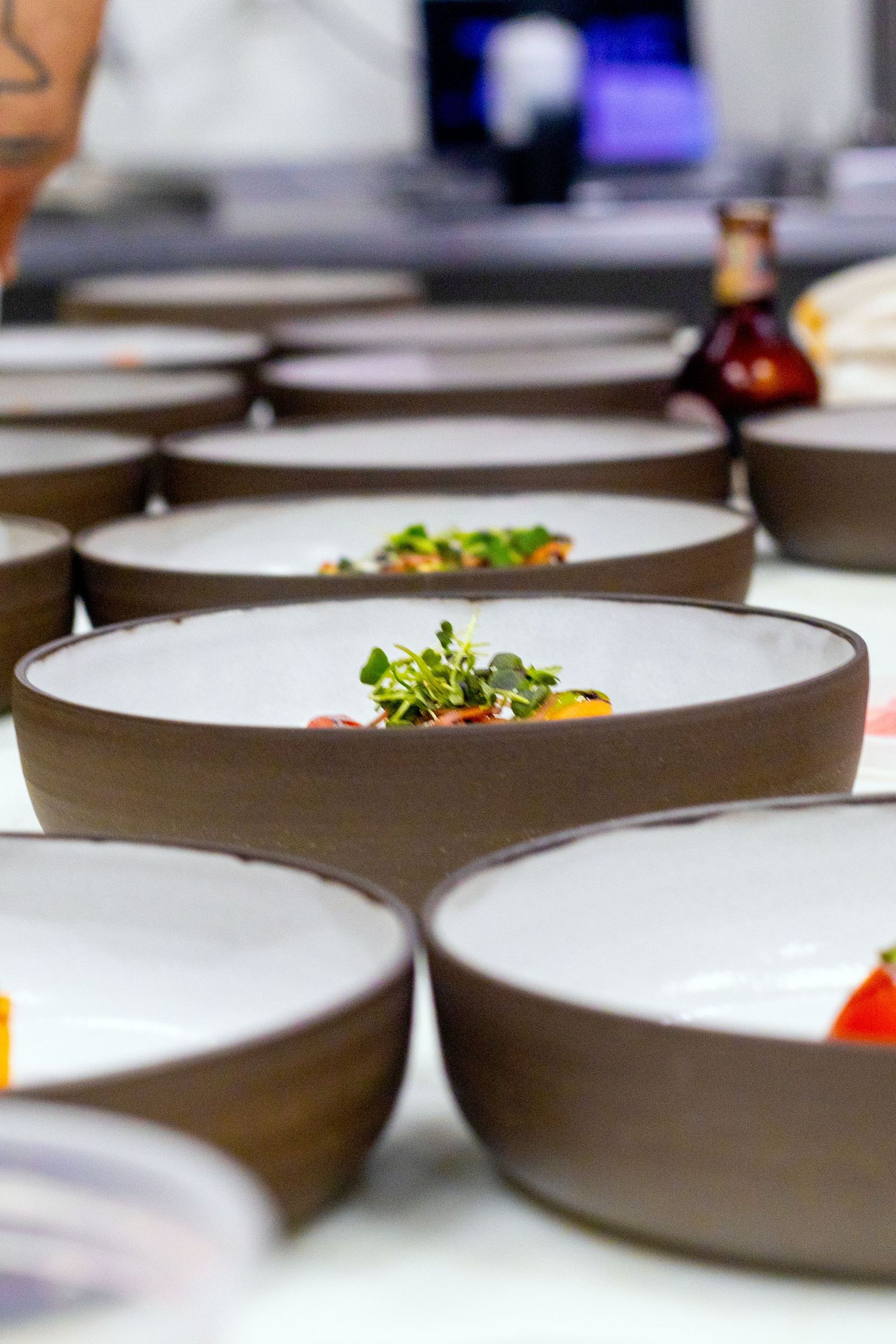 Rows of elegant brown and white ceramic bowls with gourmet microgreen garnished dishes at a fine dining restaurant.