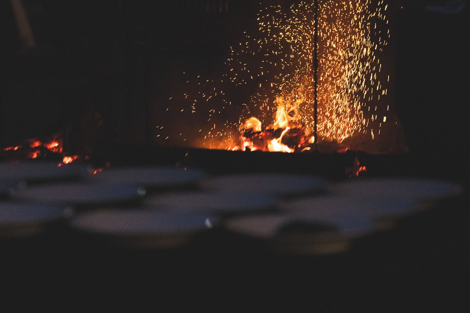 Dramatic fire pit with glowing embers and sparks flying at an outdoor evening wedding event.