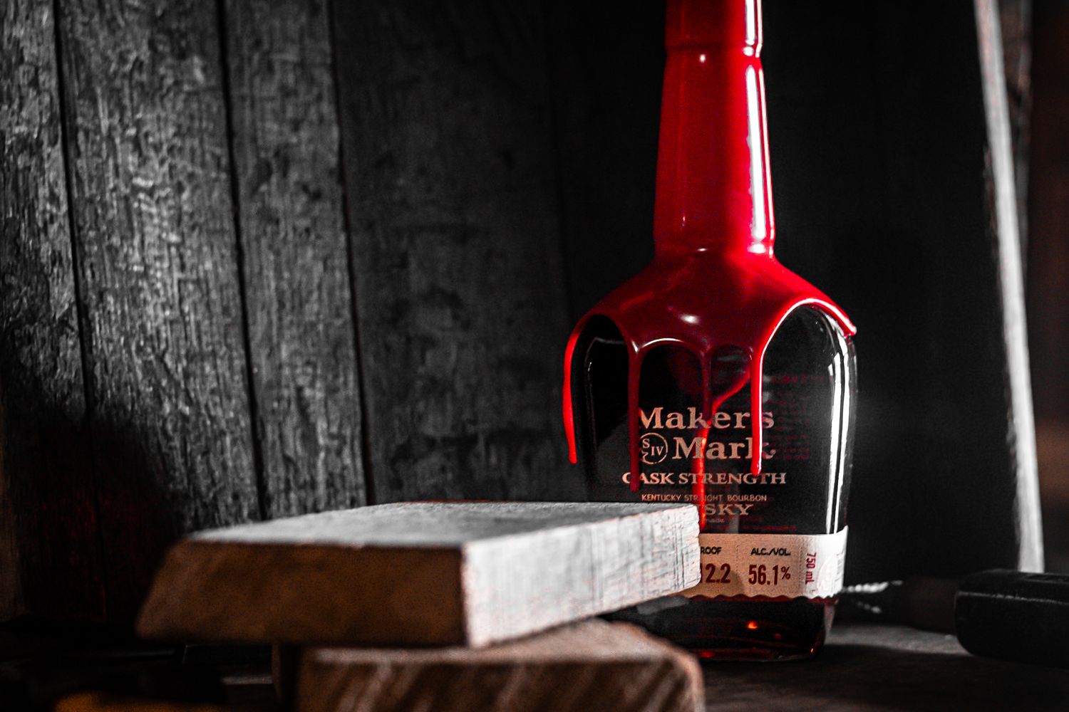 Maker's Mark Cask Strength bourbon whiskey bottle with red wax seal displayed on rustic wooden surface in dramatic lighting.