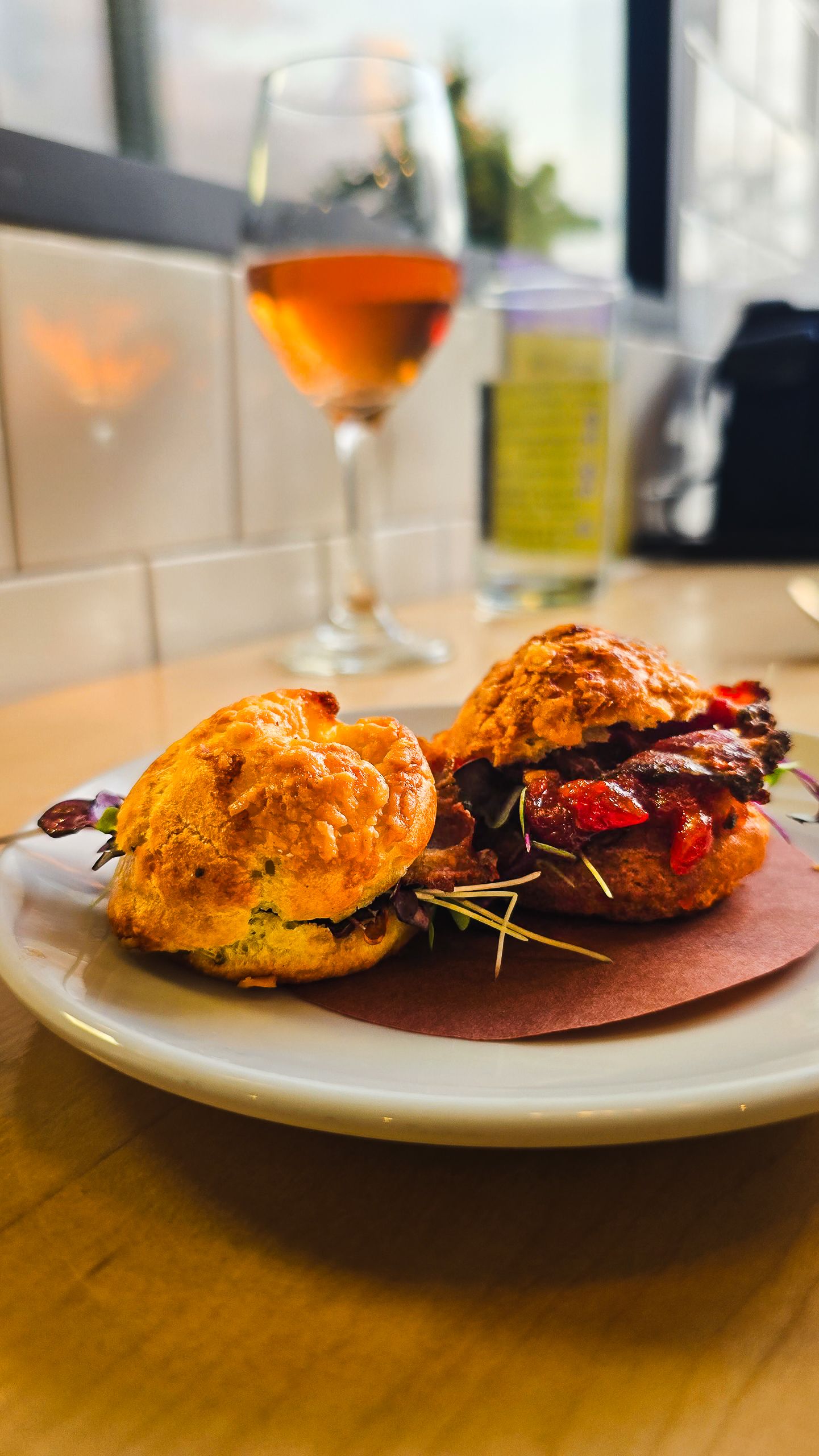Savory biscuit sandwich filled with roasted meat and tomatoes, served with a glass of rose wine on a wooden table.