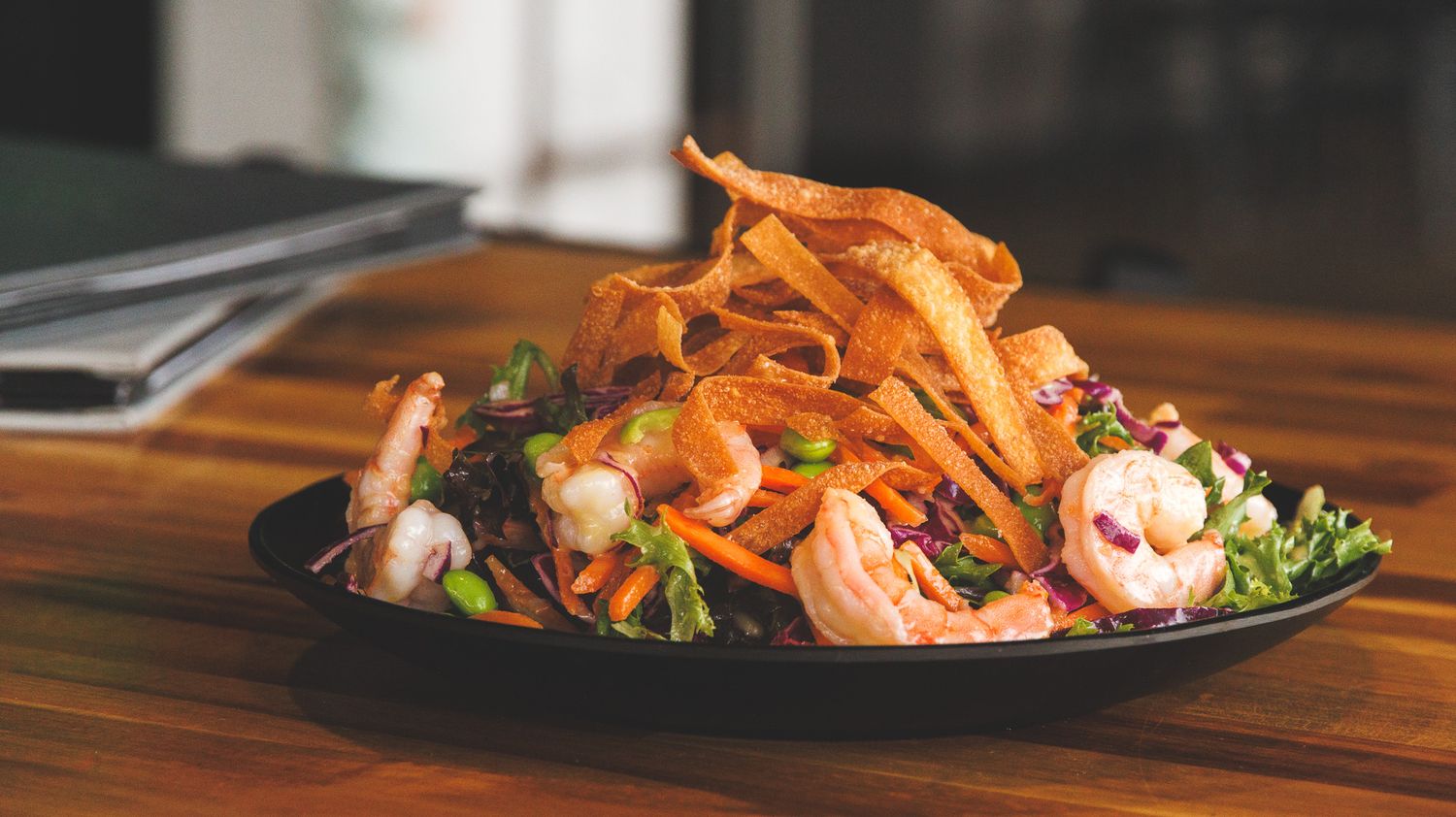 Fresh shrimp salad with crispy wonton strips, mixed greens, and red cabbage served on a black plate.