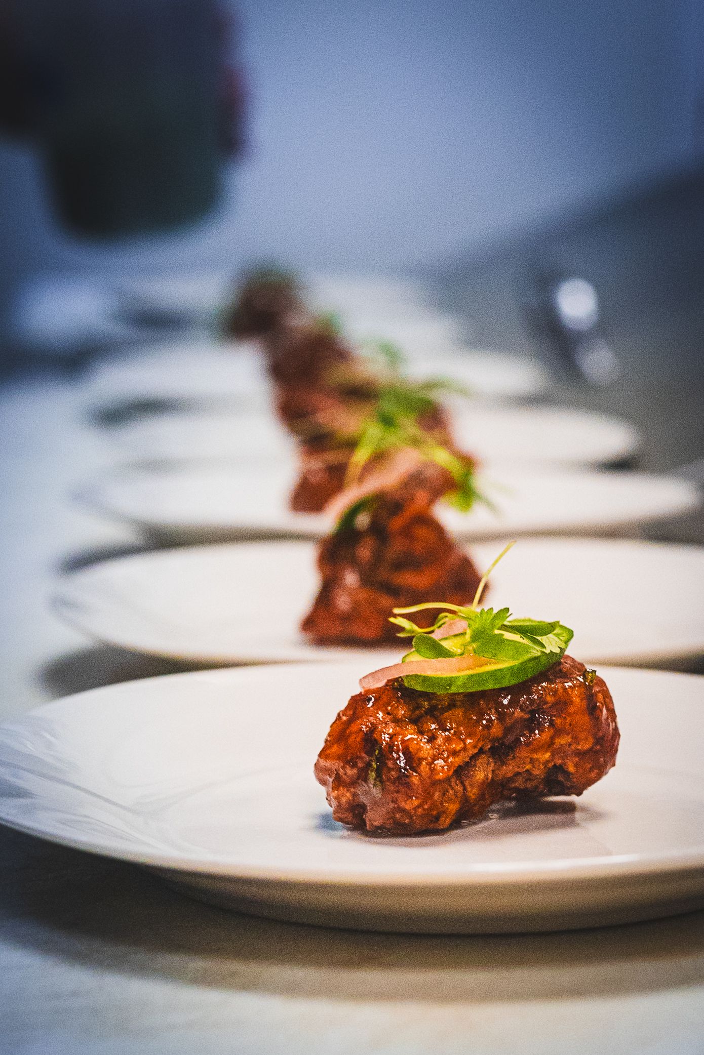 Elegant plated appetizers with glazed meat topped with avocado and microgreens on white plates in a fine dining restaurant.