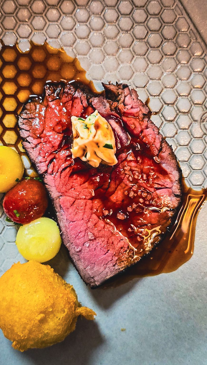 Perfectly cooked medium-rare steak with compound butter, glazed cherry tomatoes, and fried croquette.