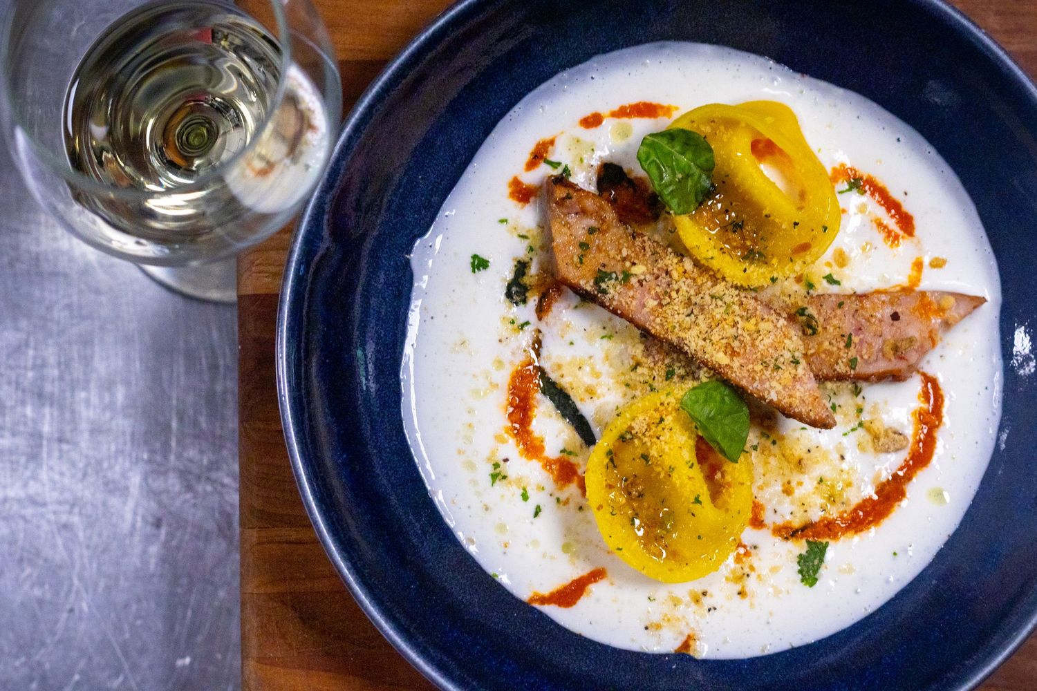 Elegant plated salmon dish with yellow tomatoes in creamy sauce, garnished with herbs and paprika, served in a blue bowl.