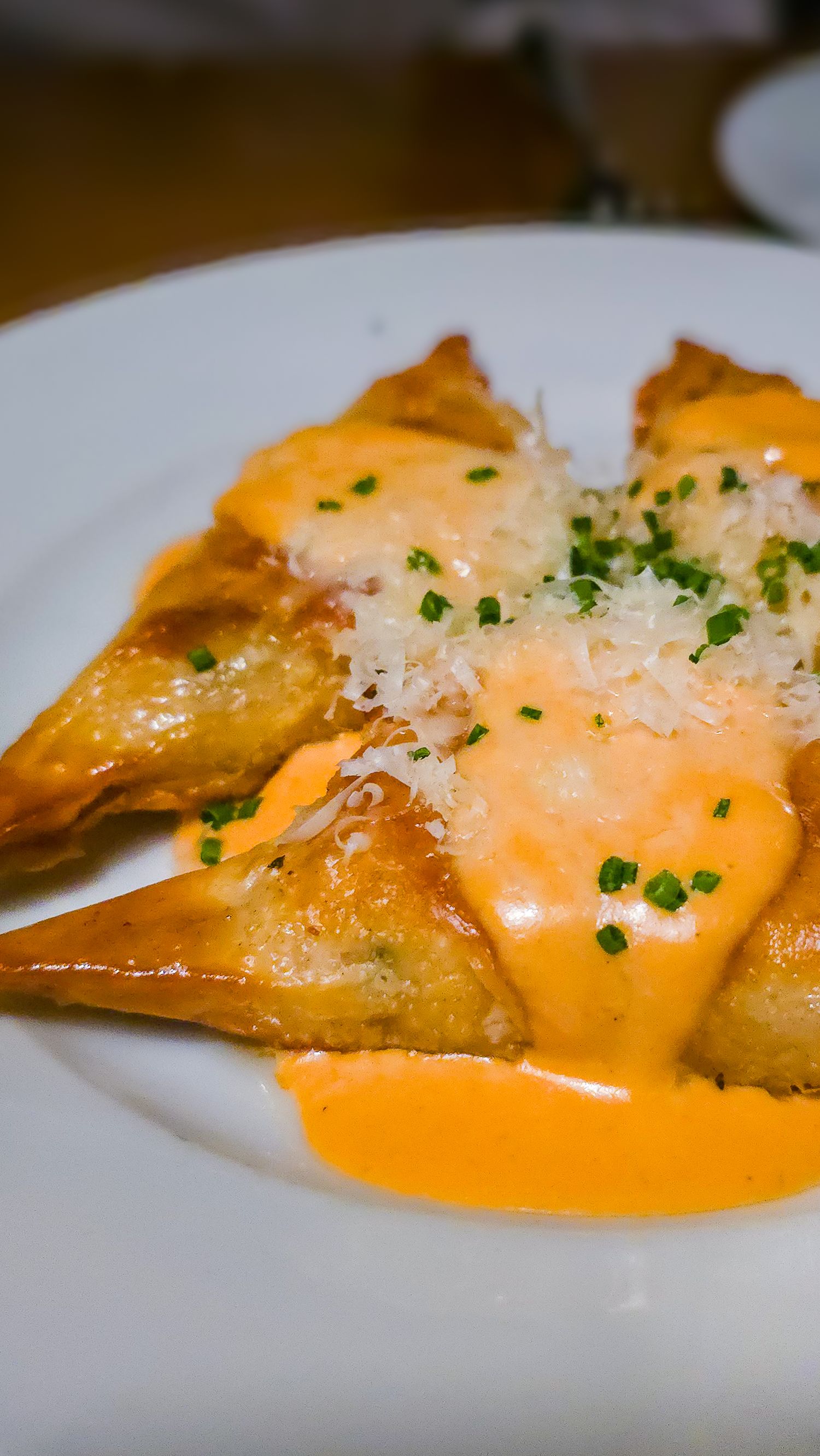 Golden fried pasta parcels topped with creamy orange sauce, grated cheese, and fresh chives on white plate.