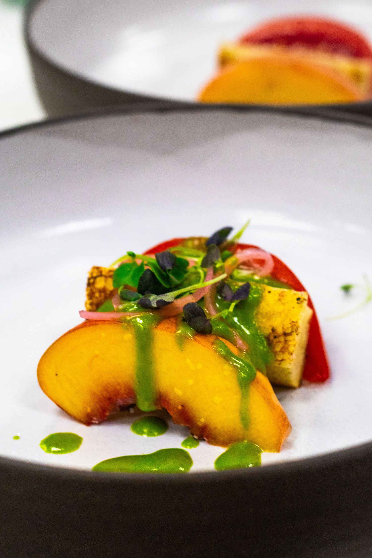 Elegant plated dish featuring sliced peaches with green herb sauce and microgreens on a white ceramic bowl.