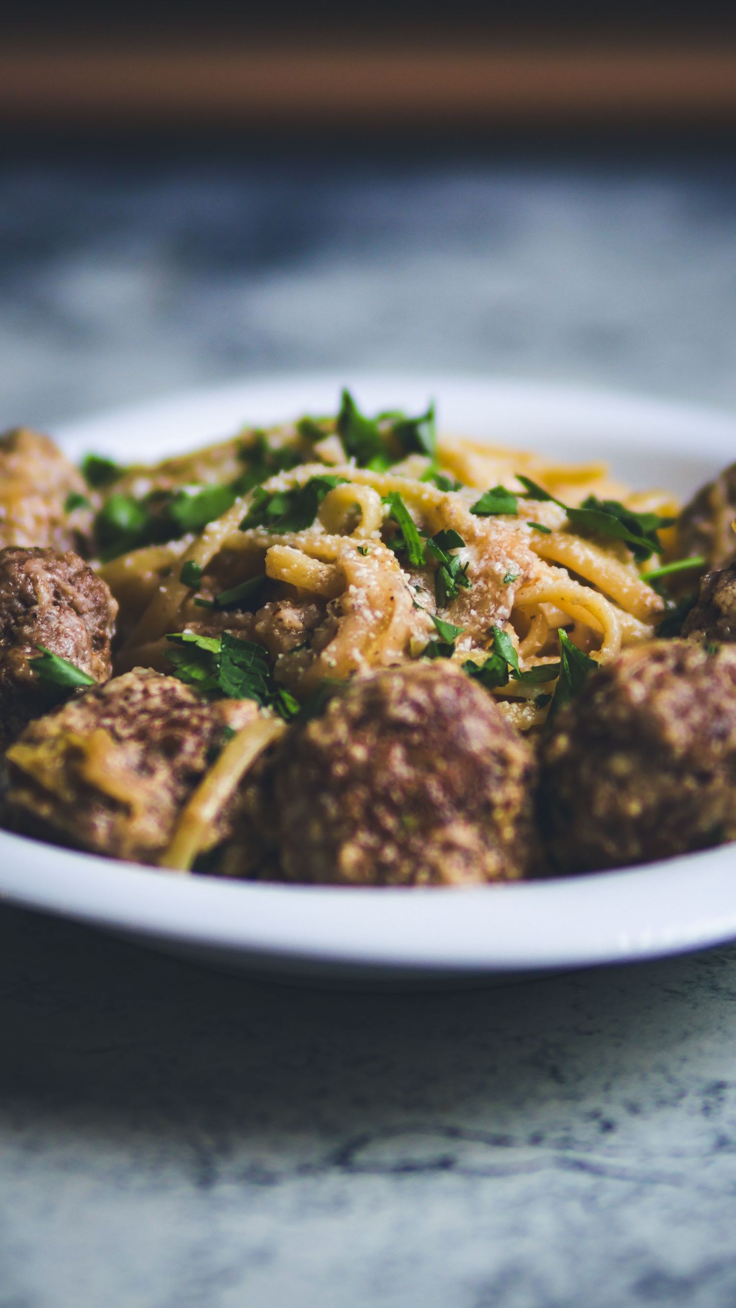 Close-up of breaded meatballs served over creamy pasta with fresh parsley garnish on a white plate.