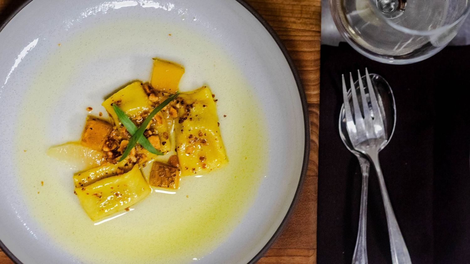 A gourmet pasta dish with yellow butter sauce, fresh herbs, and spices served in a white bowl on a wooden table.