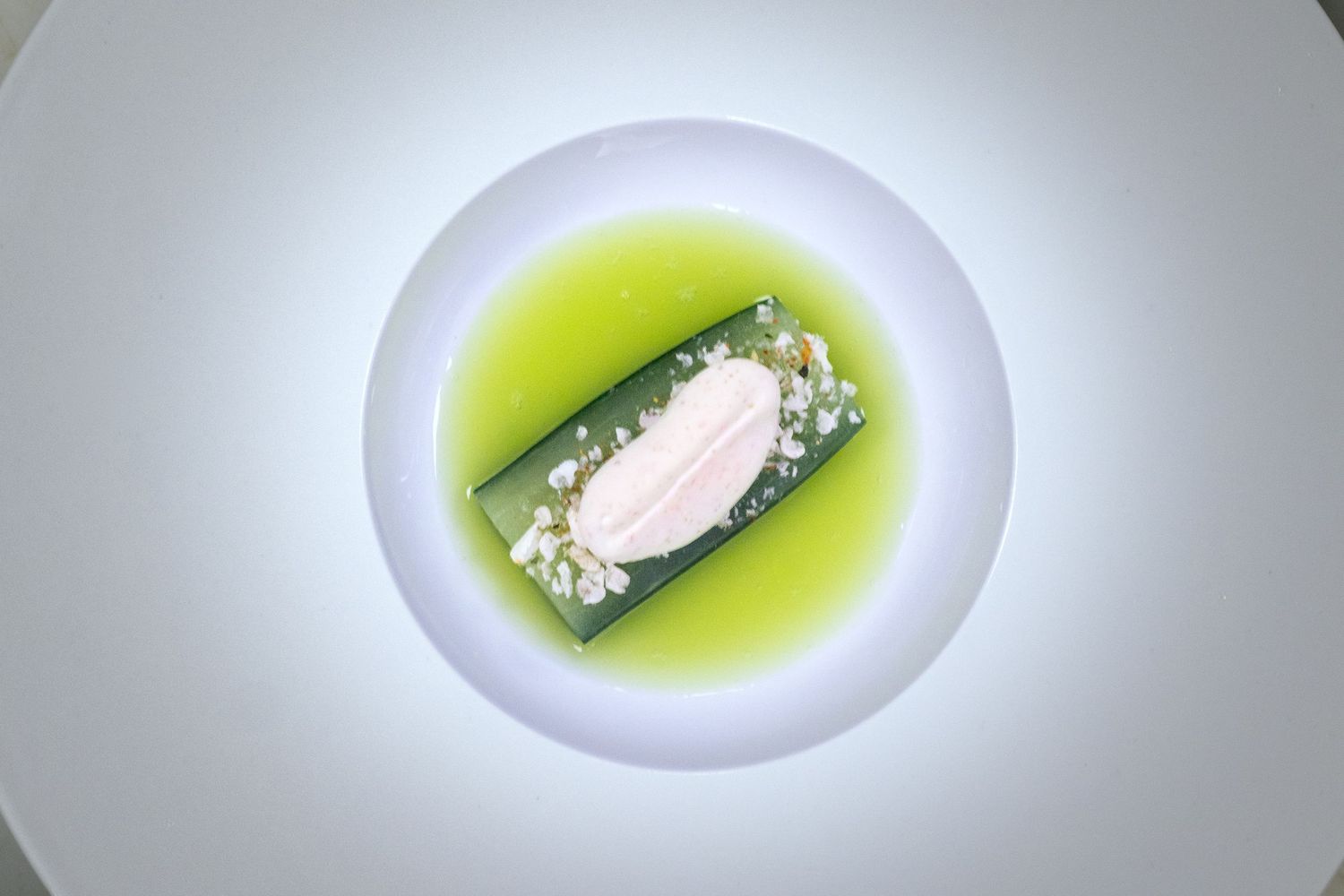 Elegant fine dining dish with white fish fillet on green cucumber, herb garnish, and vibrant green sauce on white plate.