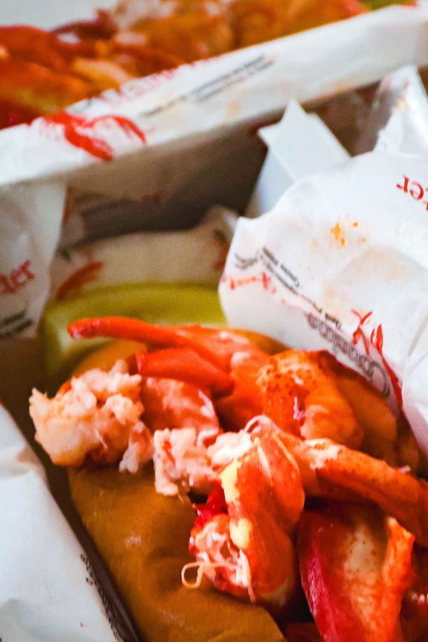 Fresh cooked lobster claws and meat served in takeout containers with white paper wrapping.