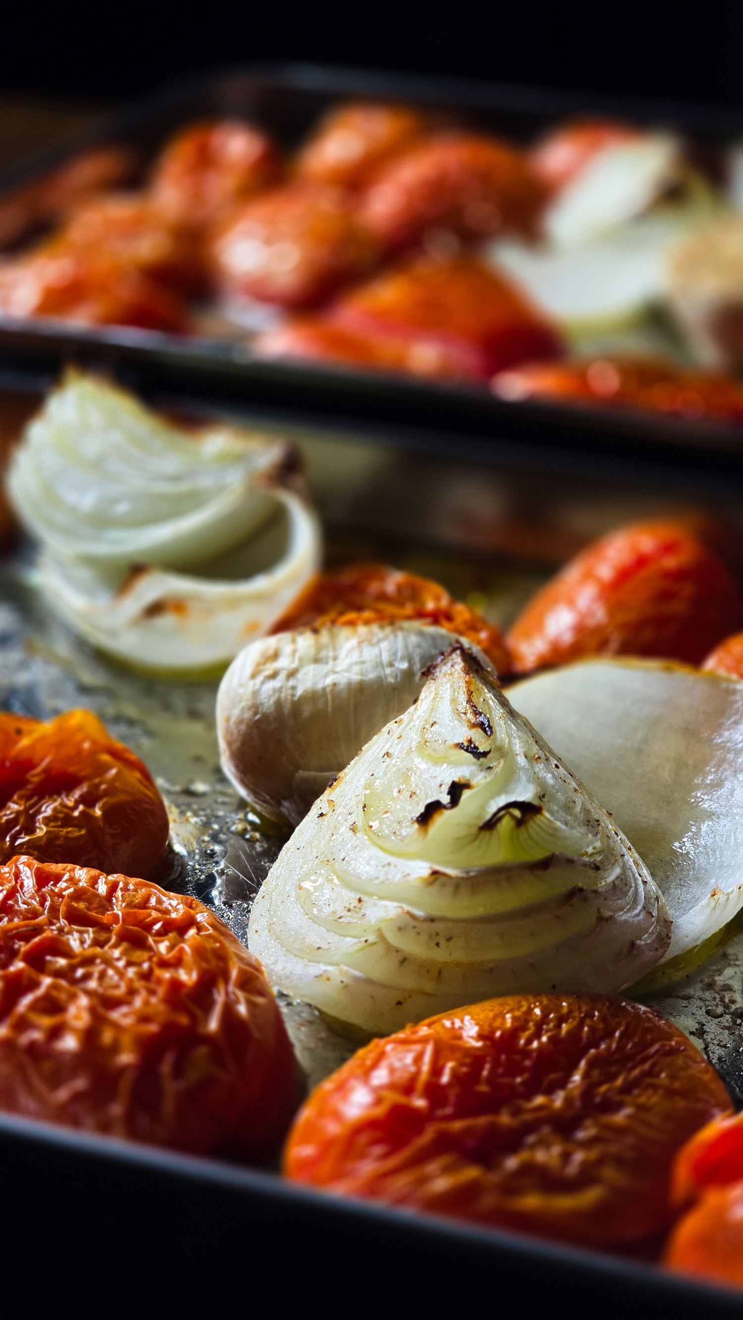 Roasted tomatoes and onions on a baking sheet, caramelized and golden with herbs and olive oil.