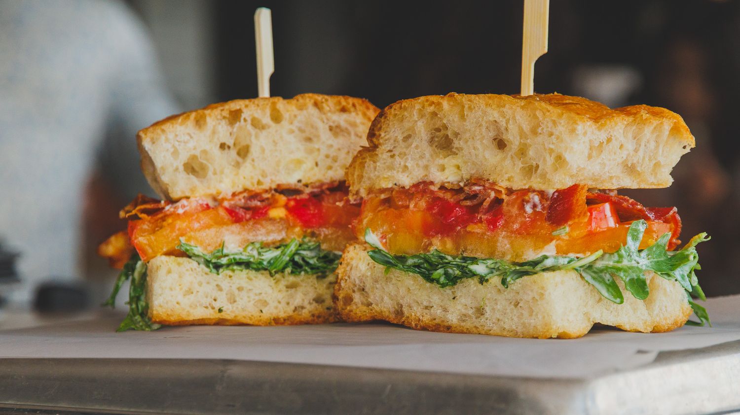 A sliced ciabatta sandwich with roasted red peppers, fresh arugula, and melted cheese, secured with toothpicks.