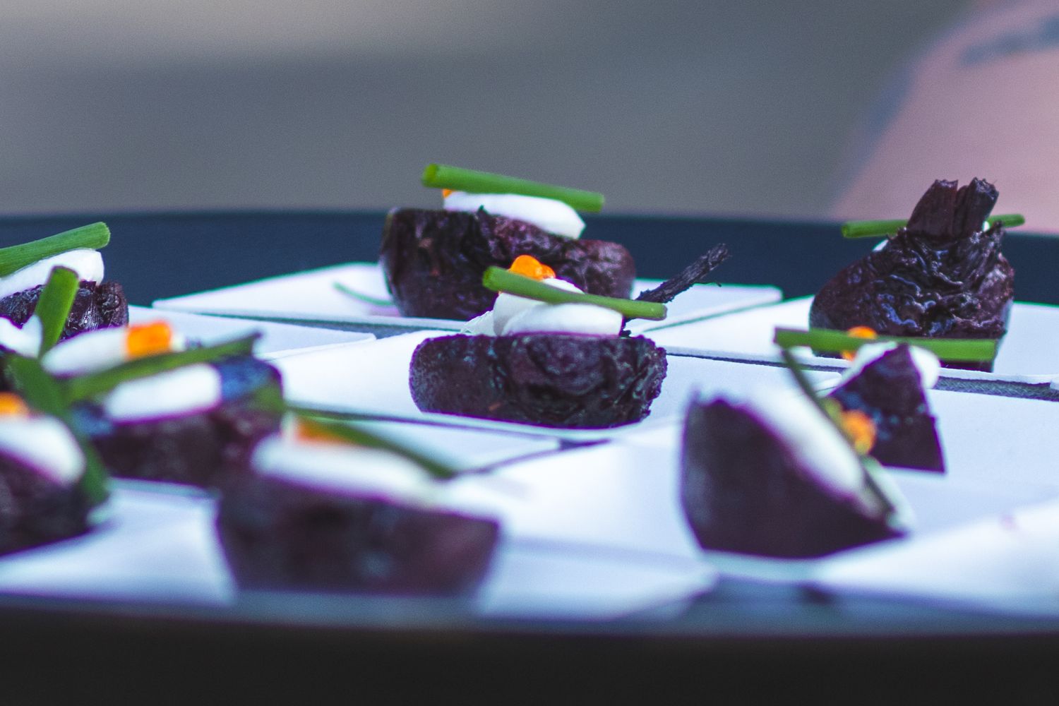Elegant dark chocolate bite-sized appetizers garnished with green chives and orange accents on a white tray.