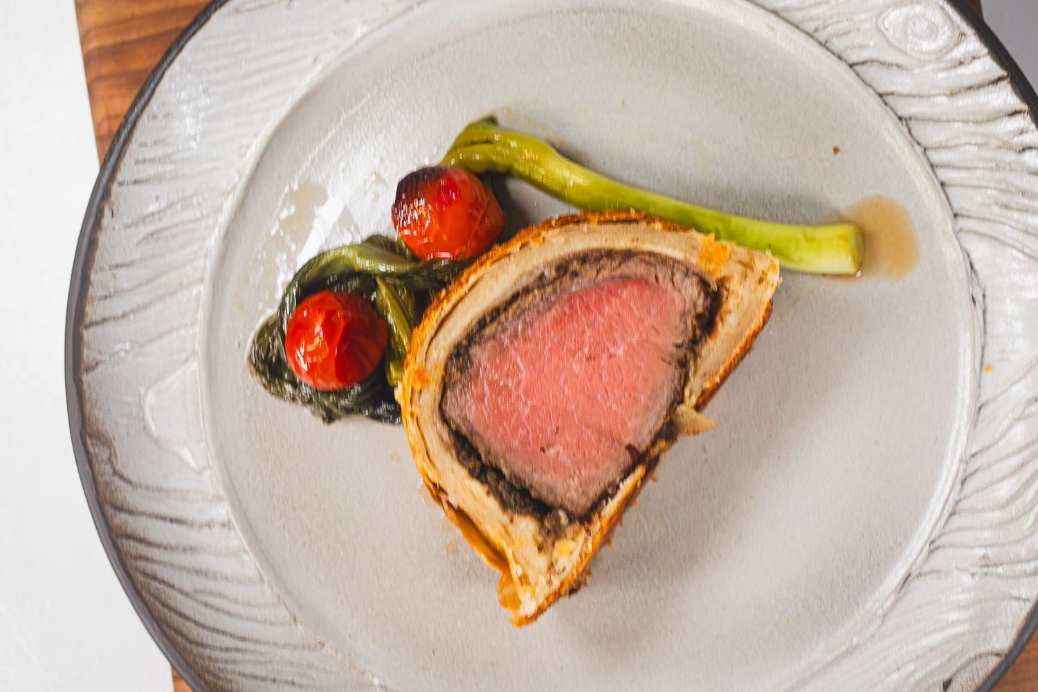 Sliced beef Wellington with pink center served with roasted cherry tomatoes and green asparagus on a white ceramic plate.