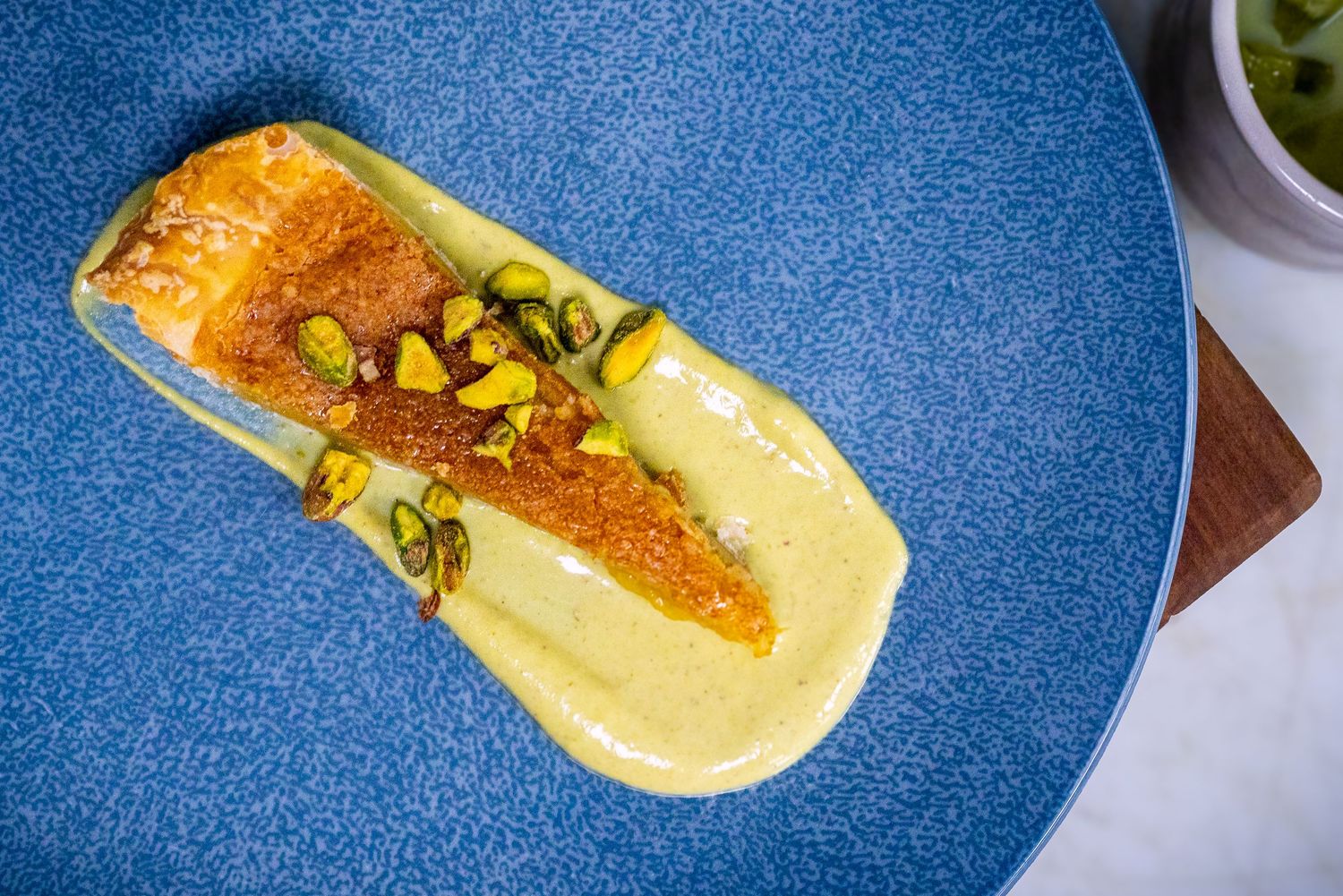 Elegant plated salmon fillet with pistachio garnish and creamy sauce on a blue ceramic plate.