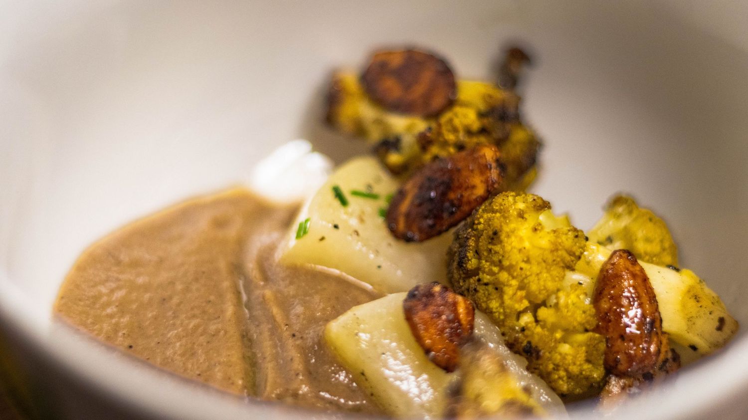 Roasted cauliflower and caramelized almonds served over smooth brown sauce in a white ceramic bowl.