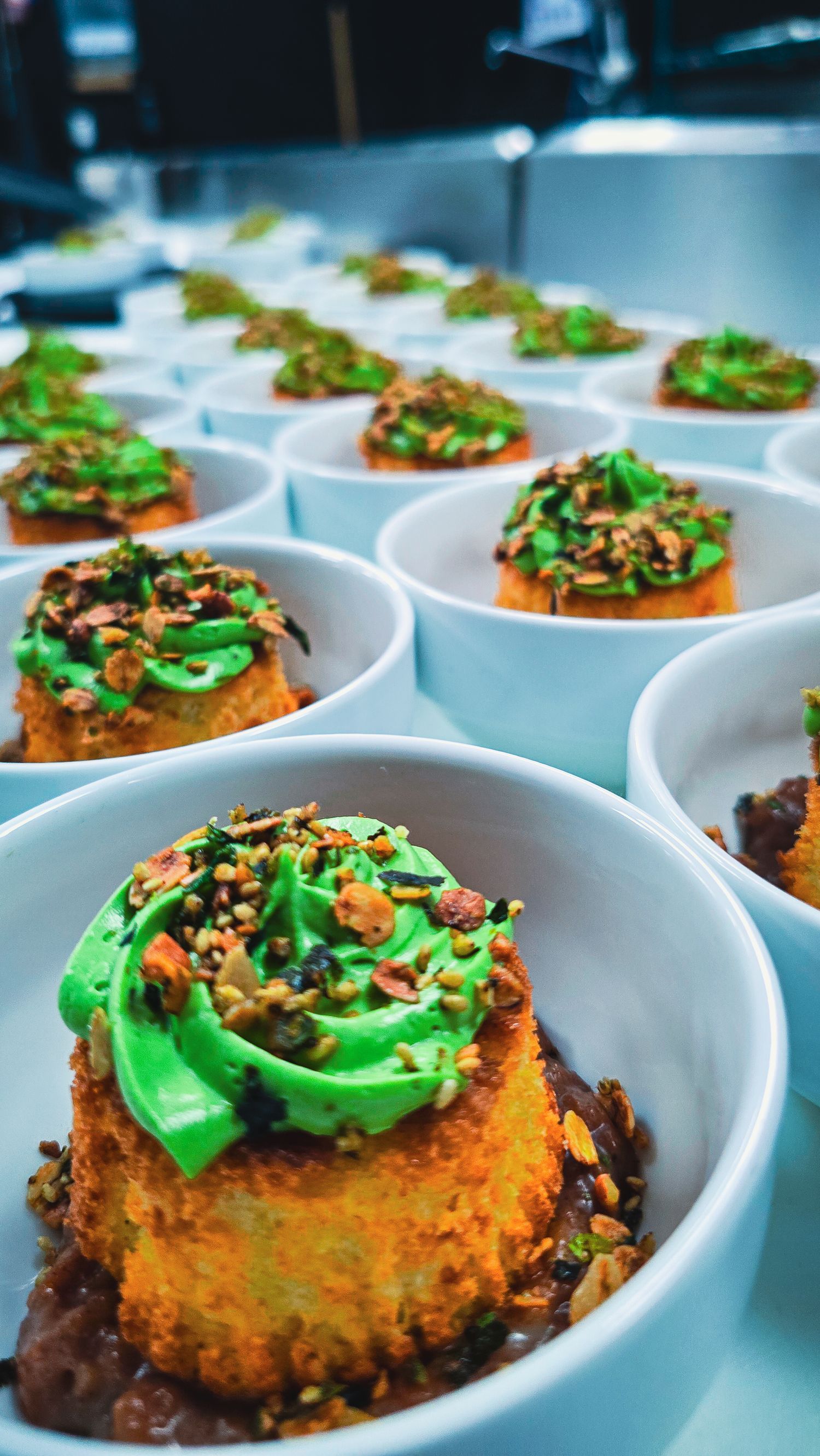 Golden cornbread cakes topped with bright green frosting and chopped nuts served in white bowls at a catered event.