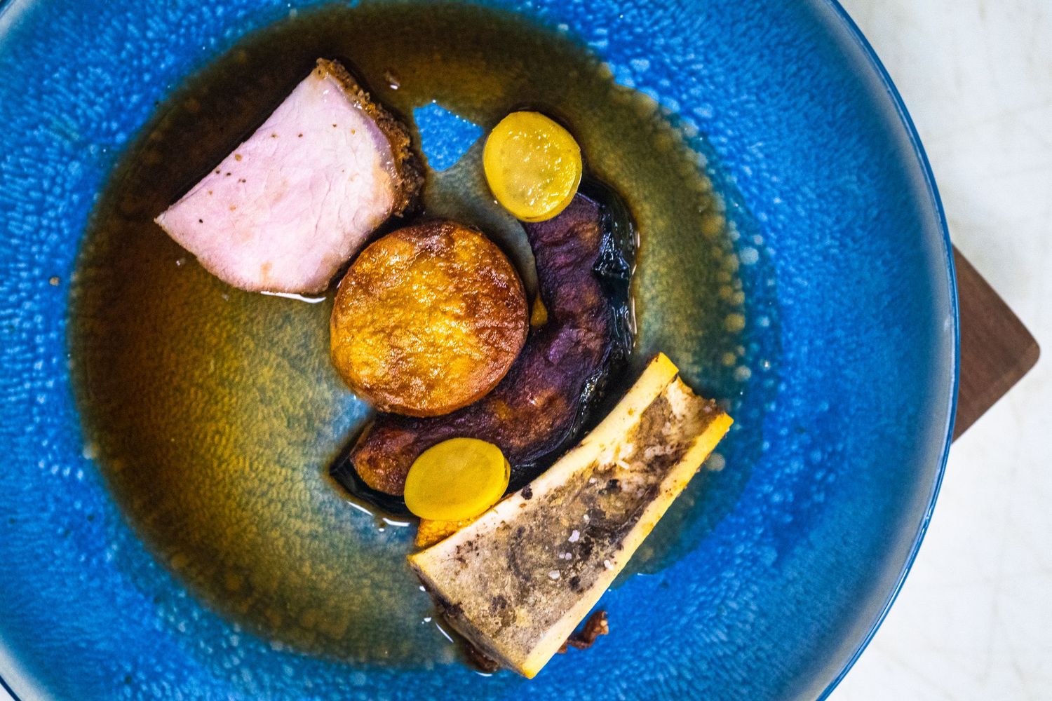 Elegant plated dish with seared meat, roasted vegetables, and sauce on a blue ceramic plate.