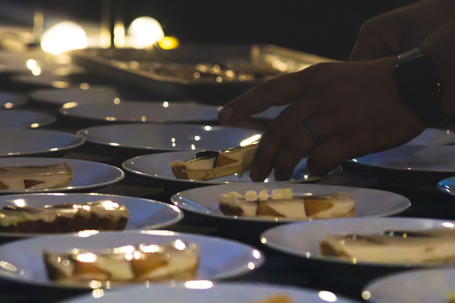 Catering staff arranging plated desserts on white dishes at a dimly lit wedding reception.