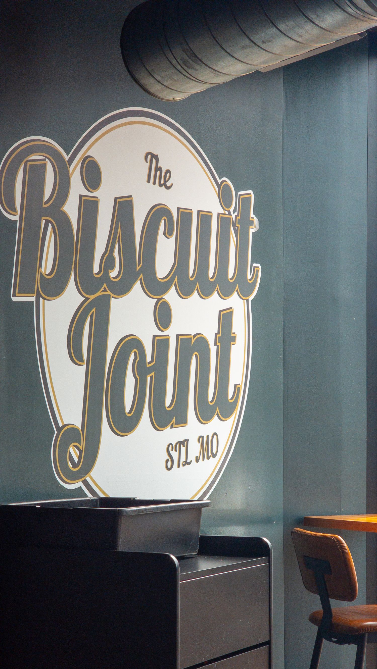 The Biscuit Joint restaurant sign in STL, MO, featuring vintage-style gold and white typography on a dark wall.