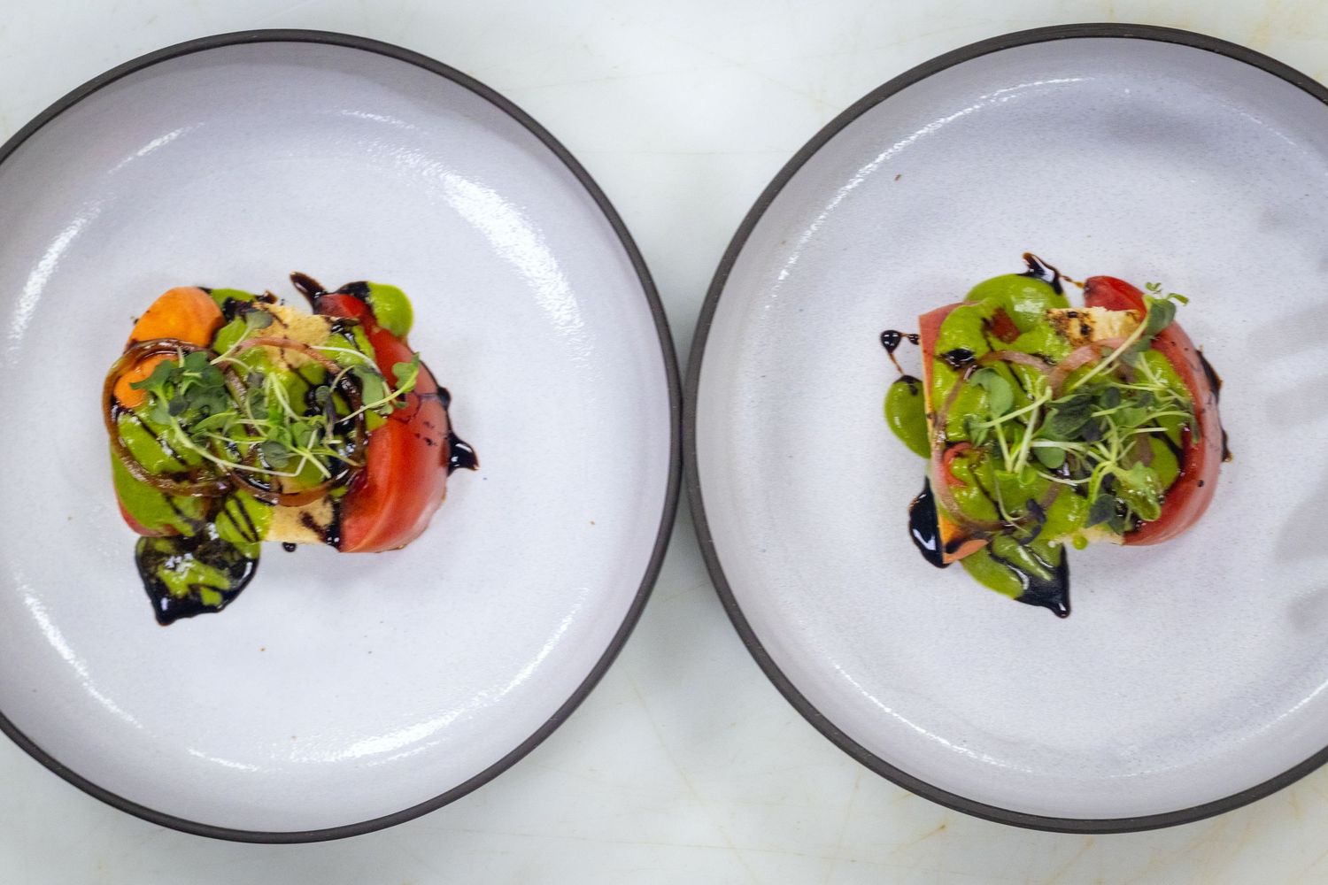 Two identical white plates topped with heirloom tomatoes, green pea puree, microgreens and balsamic glaze.