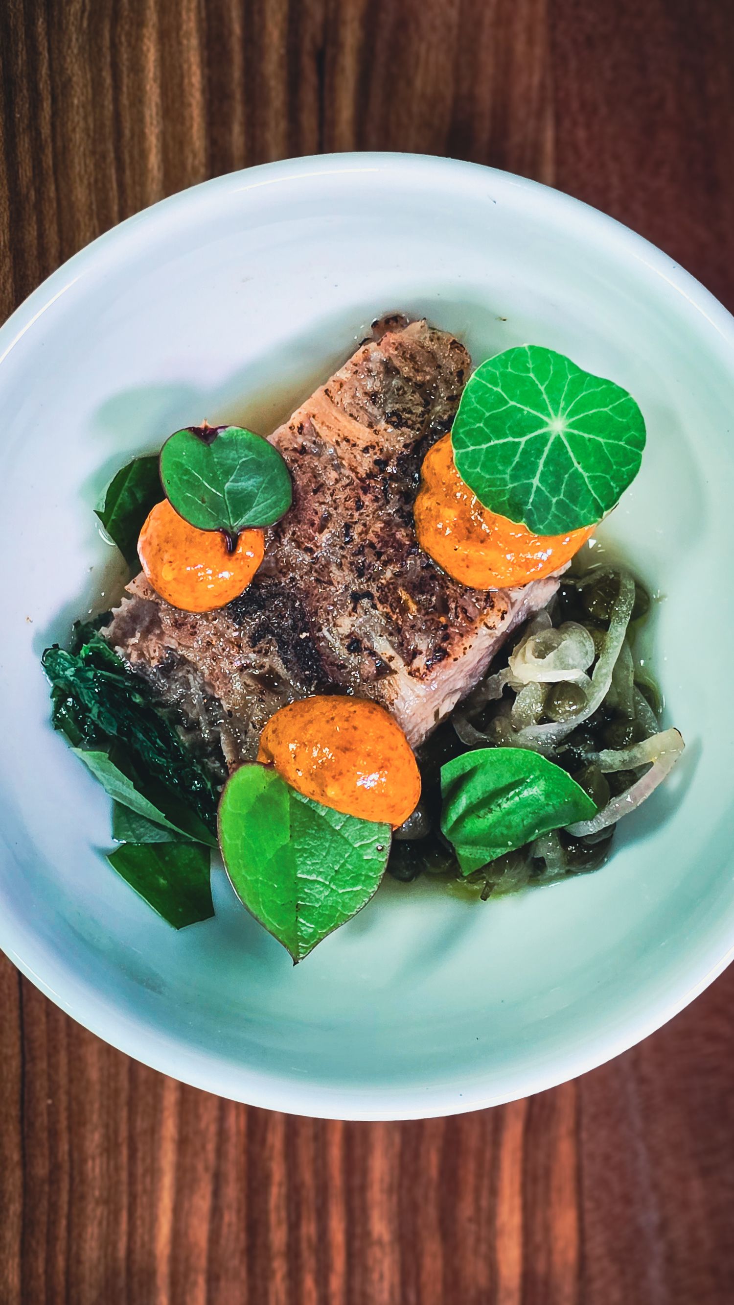 A beautifully plated seared salmon fillet garnished with nasturtium leaves and orange sauce dots in a white bowl.