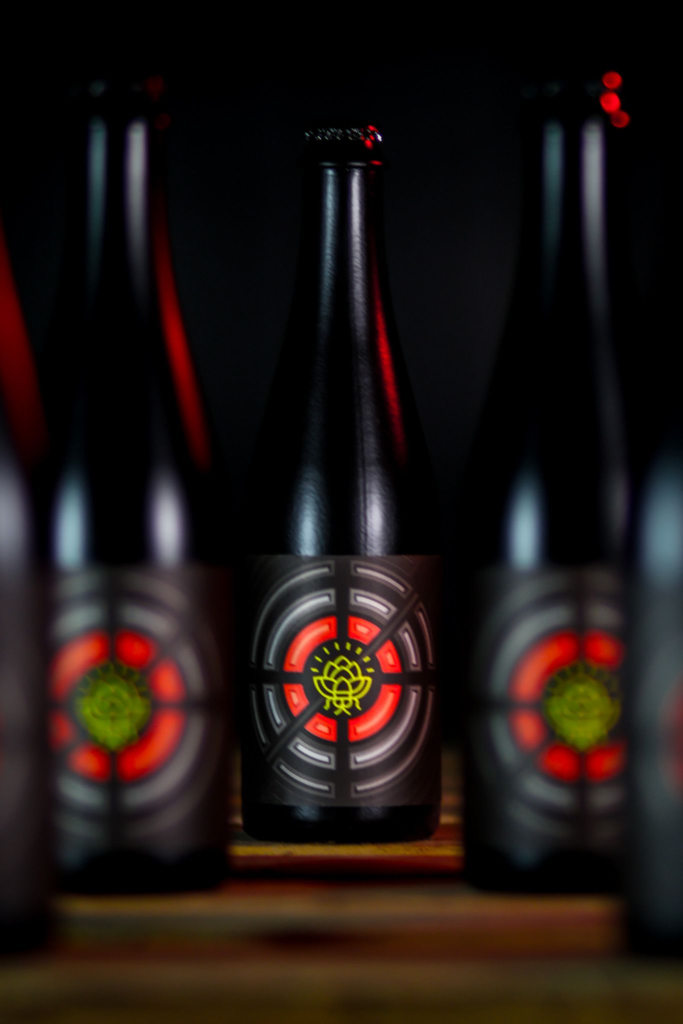 Dark craft beer bottles with striking red and yellow target-design labels displayed in dramatic low-key lighting.