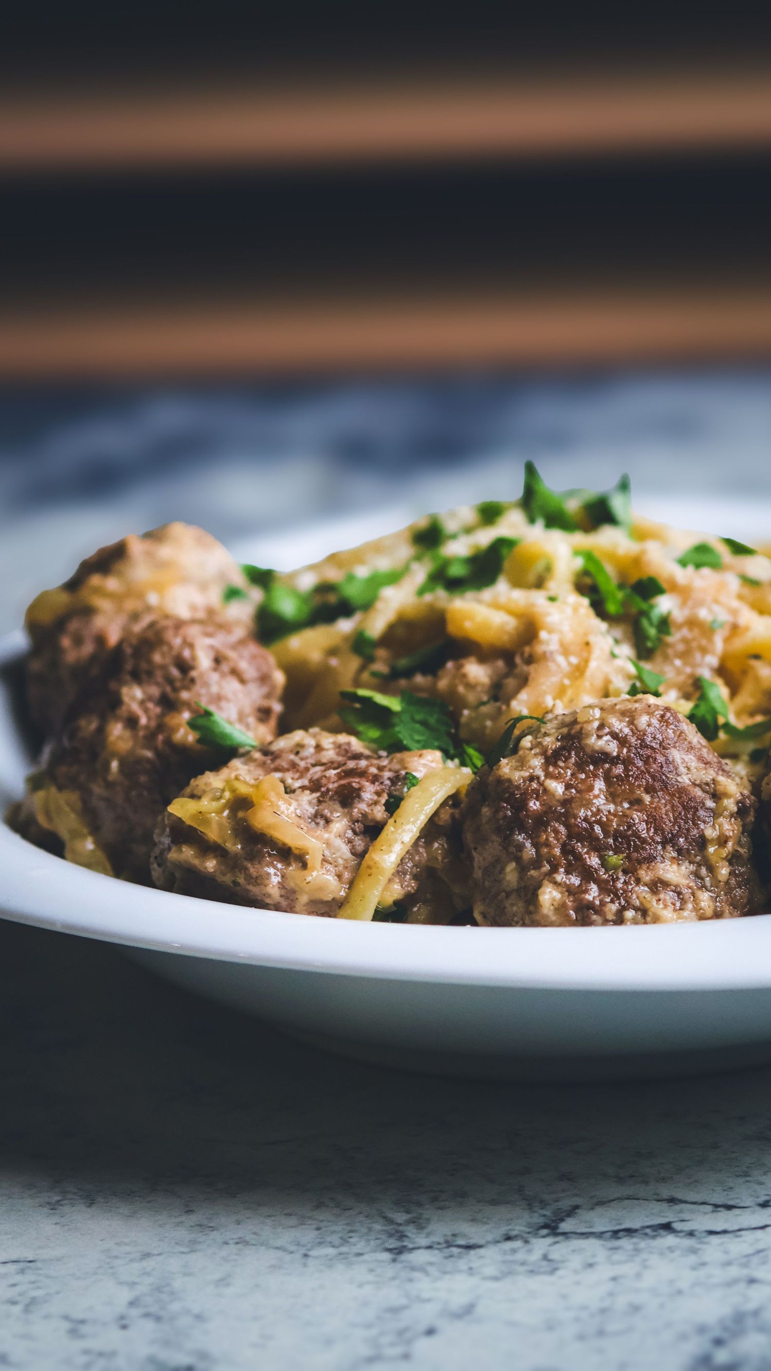 Hearty meatballs with pasta in savory sauce topped with fresh chopped parsley in white bowl.
