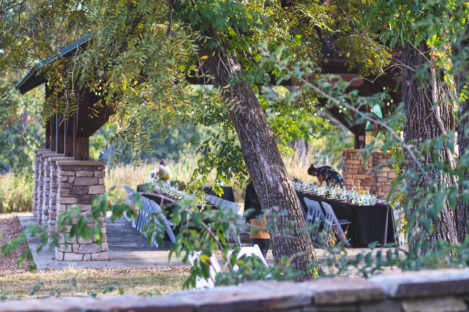 Elegant outdoor reception tables set under mature trees at a rustic garden wedding venue.