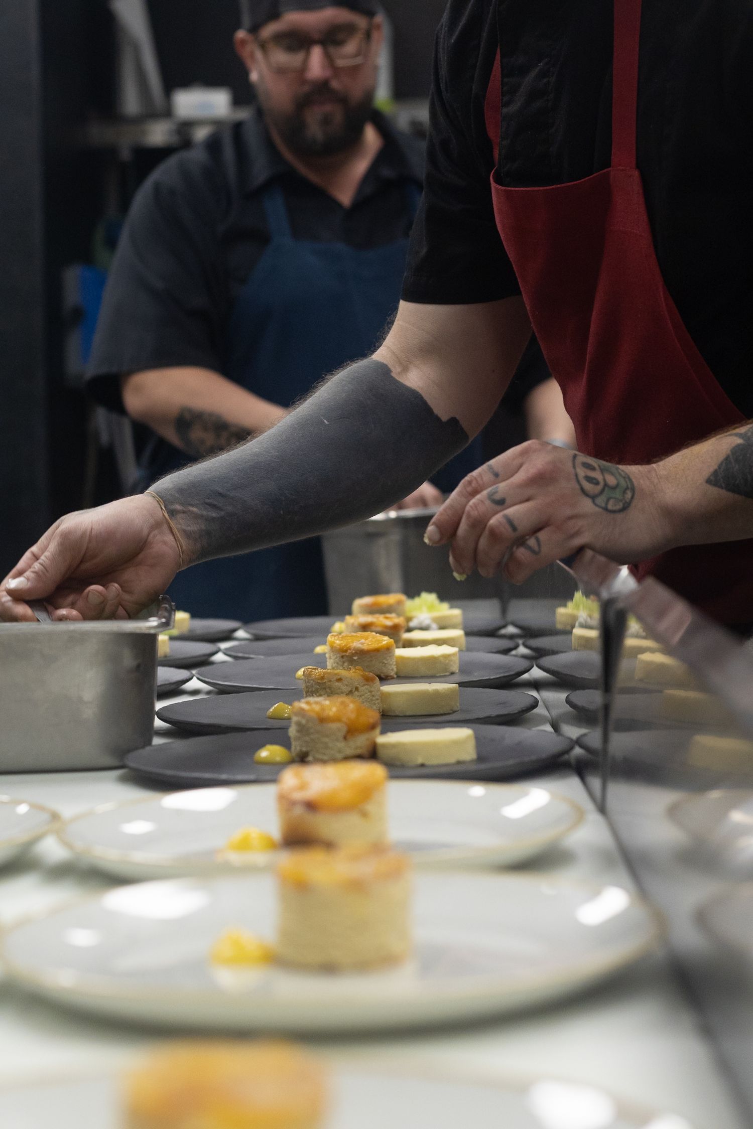 Professional chefs plating elegant appetizers on slate boards in a restaurant kitchen during dinner service.