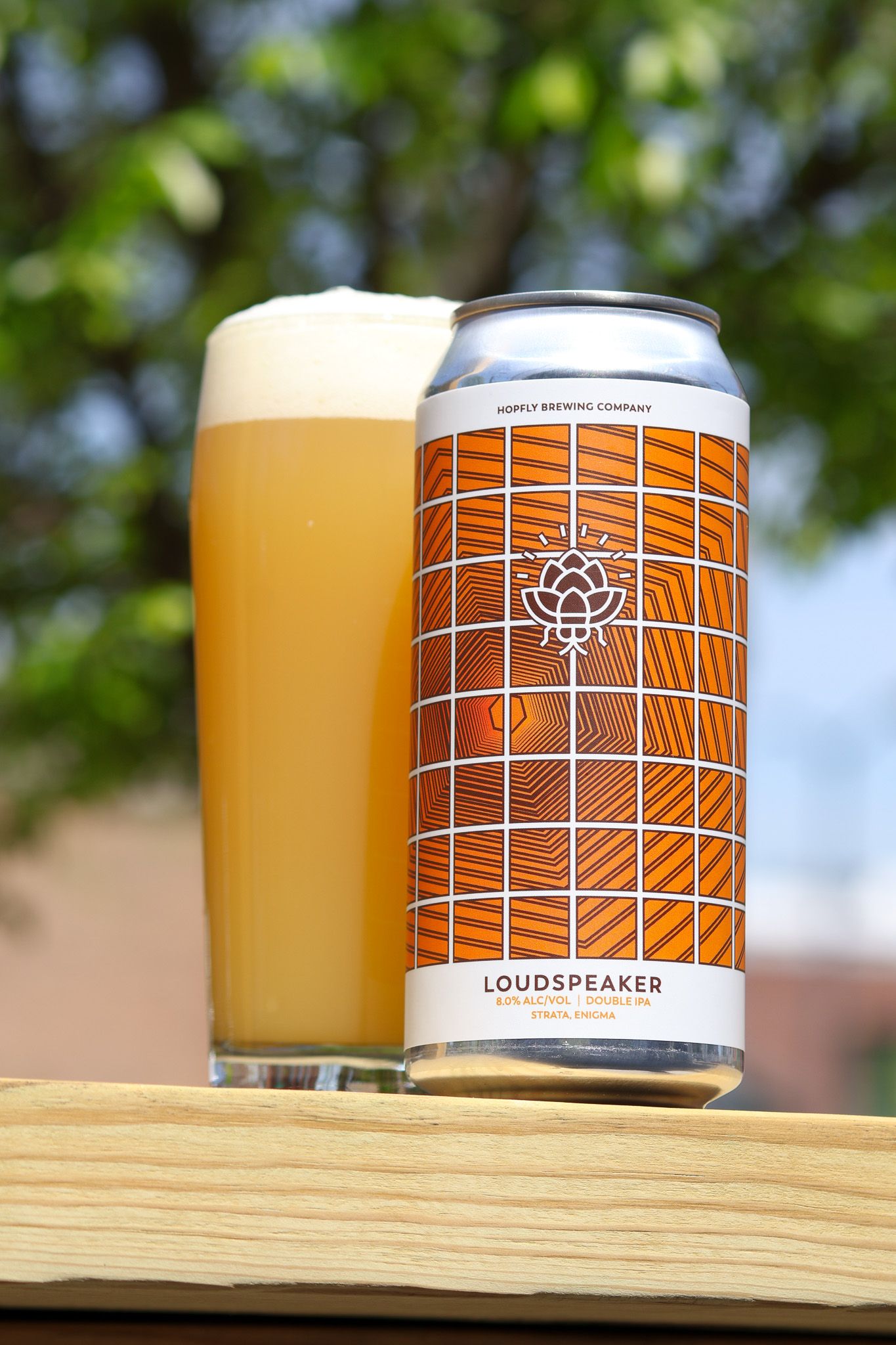 Loudspeaker IPA beer can from Mapple Brewing Company beside a full pint glass on a wooden surface outdoors.
