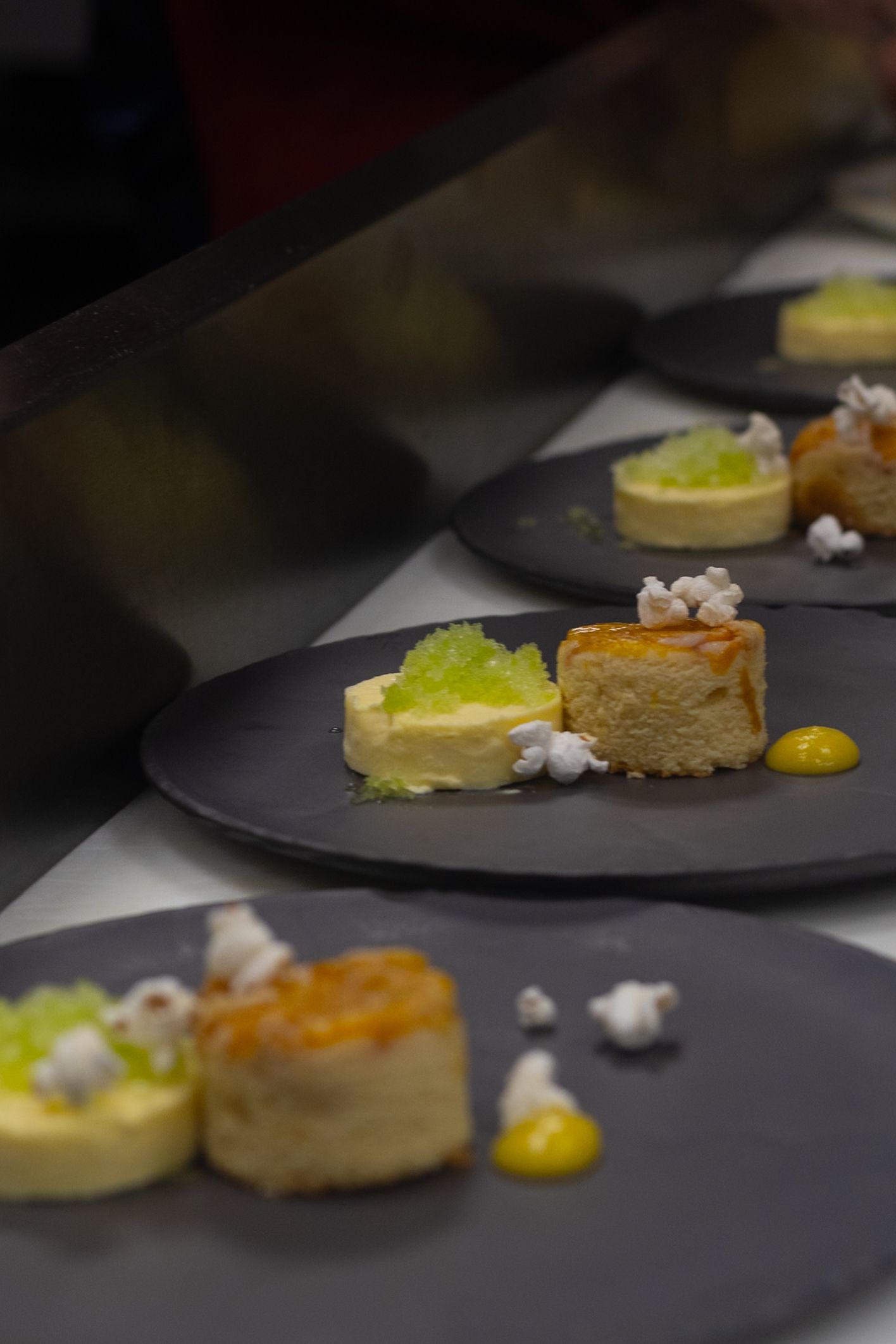 Elegant restaurant plating of golden pastry bites with green caviar, popcorn, and mustard sauce on dark slate plates.
