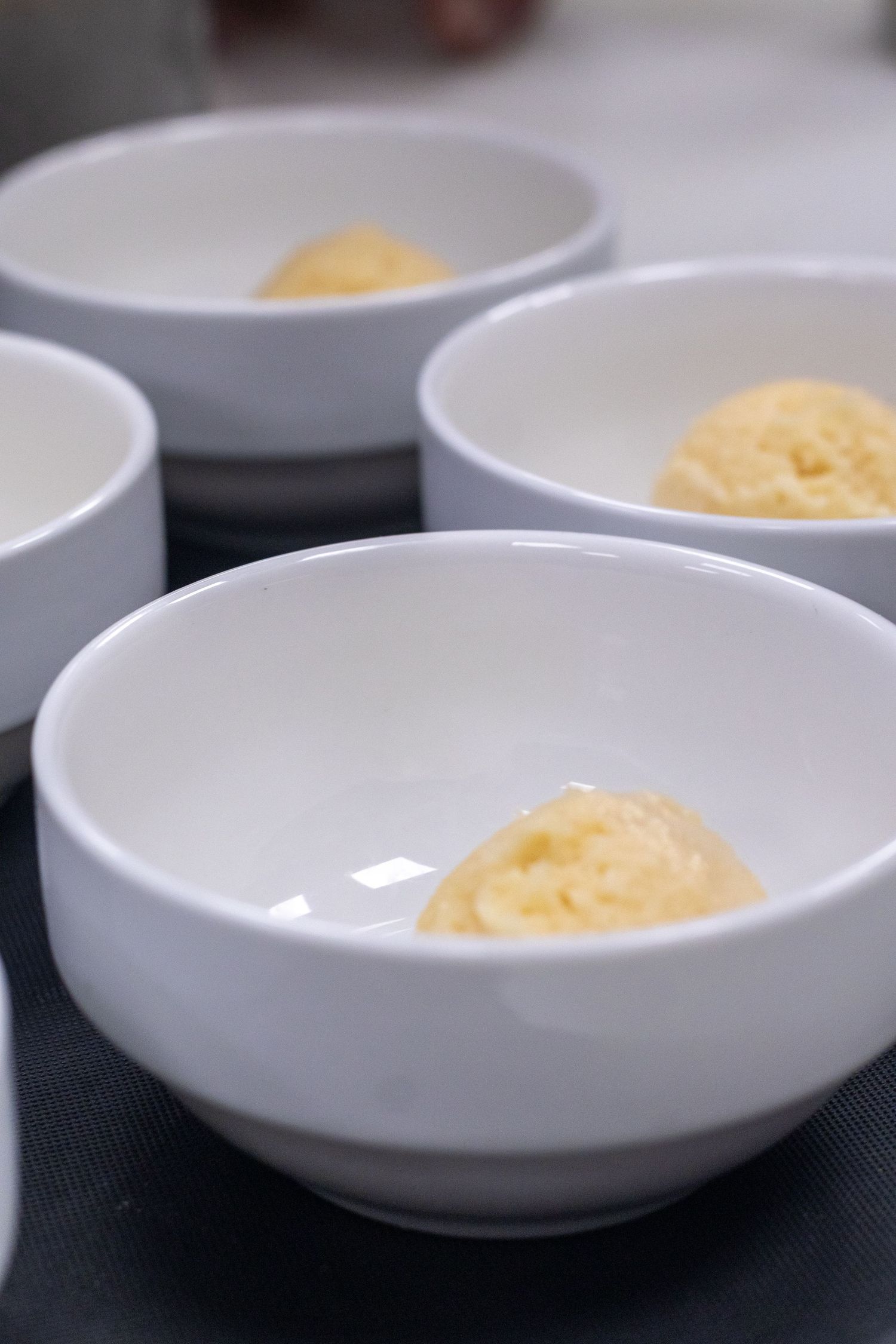 White ceramic bowls each containing a small scoop of creamy yellow food arranged on a dark surface.