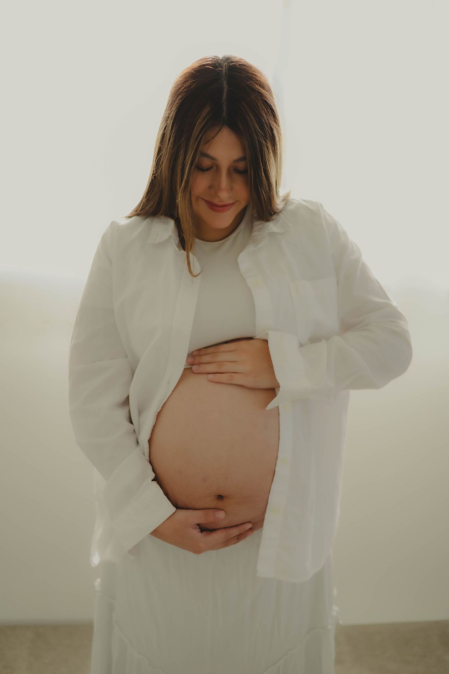 Pregnant couple in all-white studio in Culpeper, Virginia, with partner holding belly, Northern Virginia maternity photography