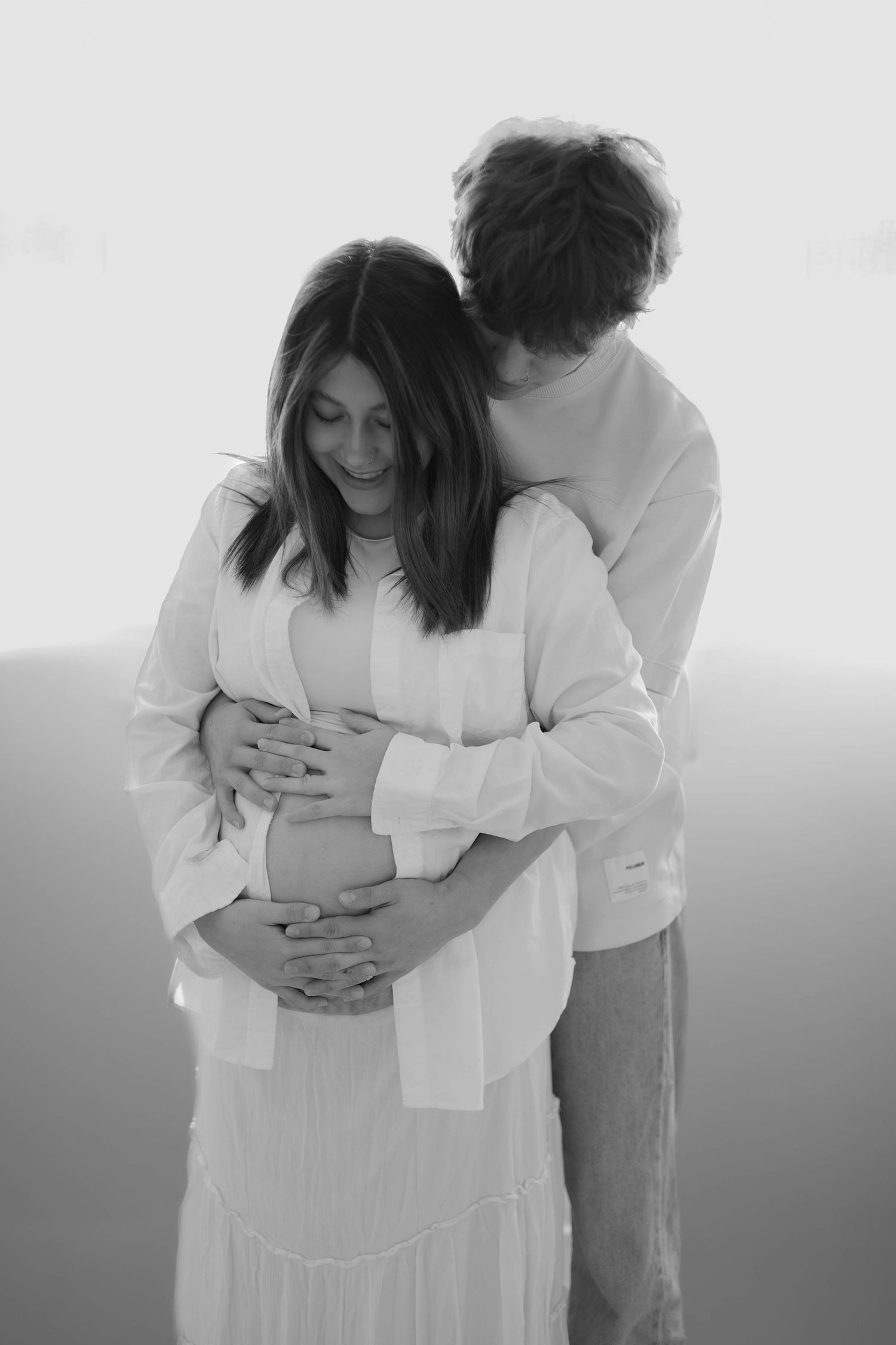 Pregnant couple in all-white studio in Culpeper, Virginia, with partner holding belly, Northern Virginia maternity photography