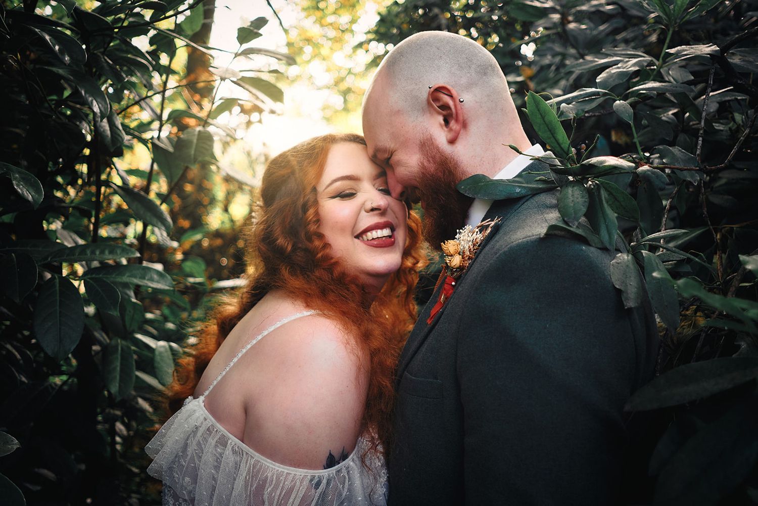 A romantic couple embraces in a lush garden setting with dappled sunlight filtering through the foliage.