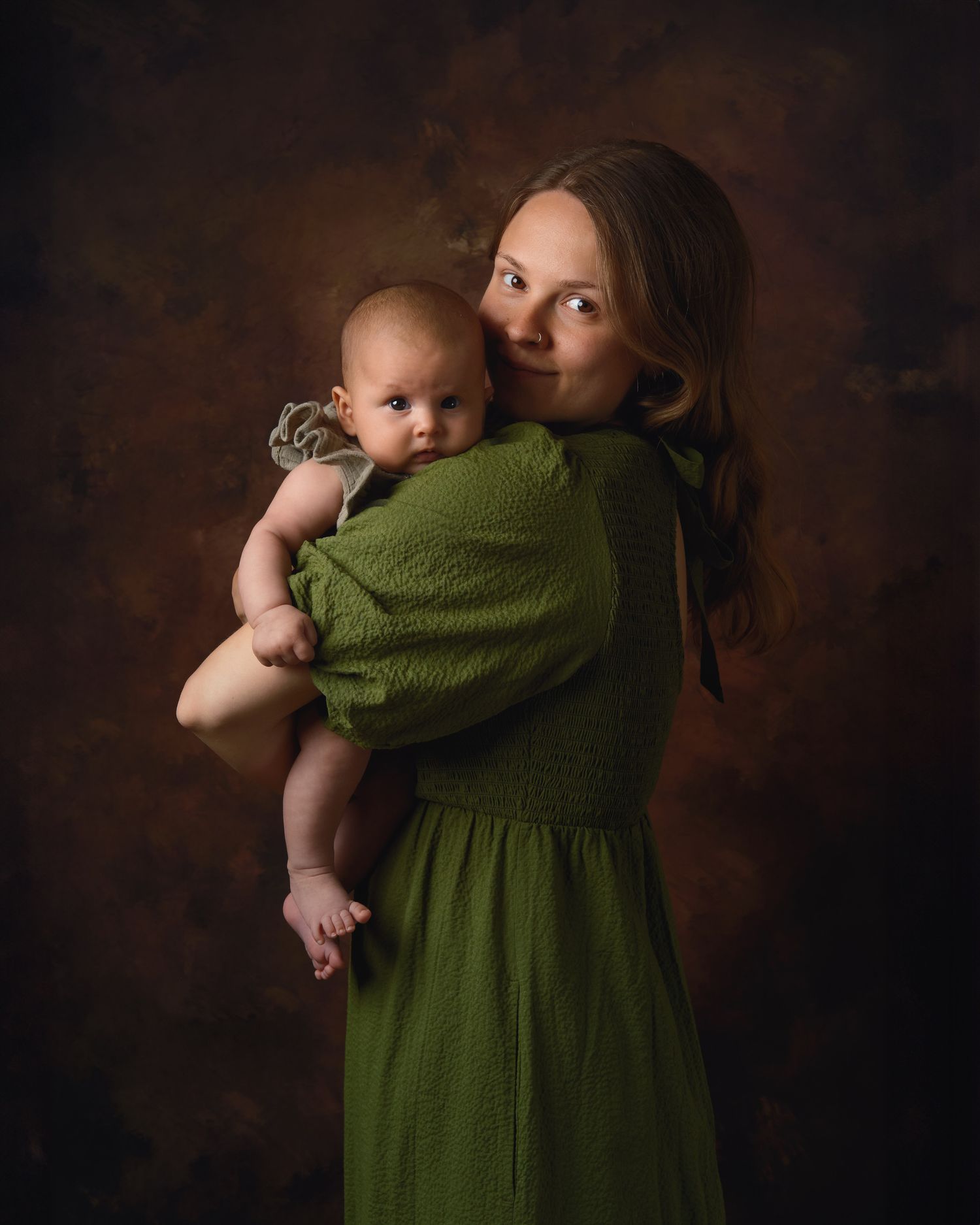A series of artistic studio portraits showing a parent and baby in a dark setting with a green dress.