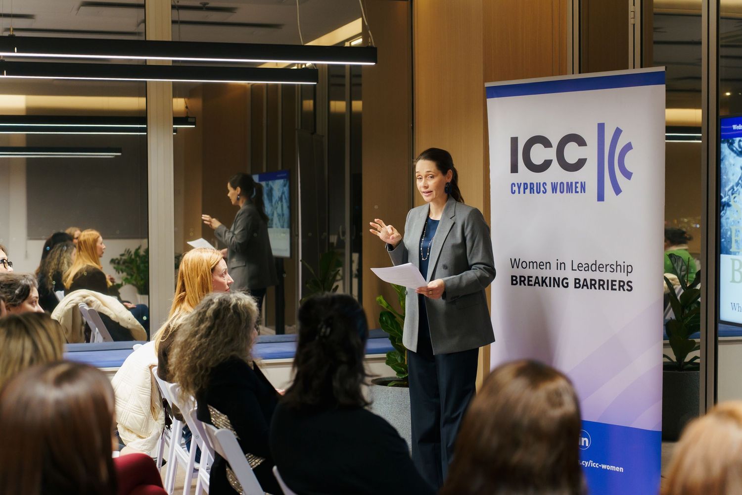 A speaker presents to an audience at a business event with an ICC banner displayed in the background.