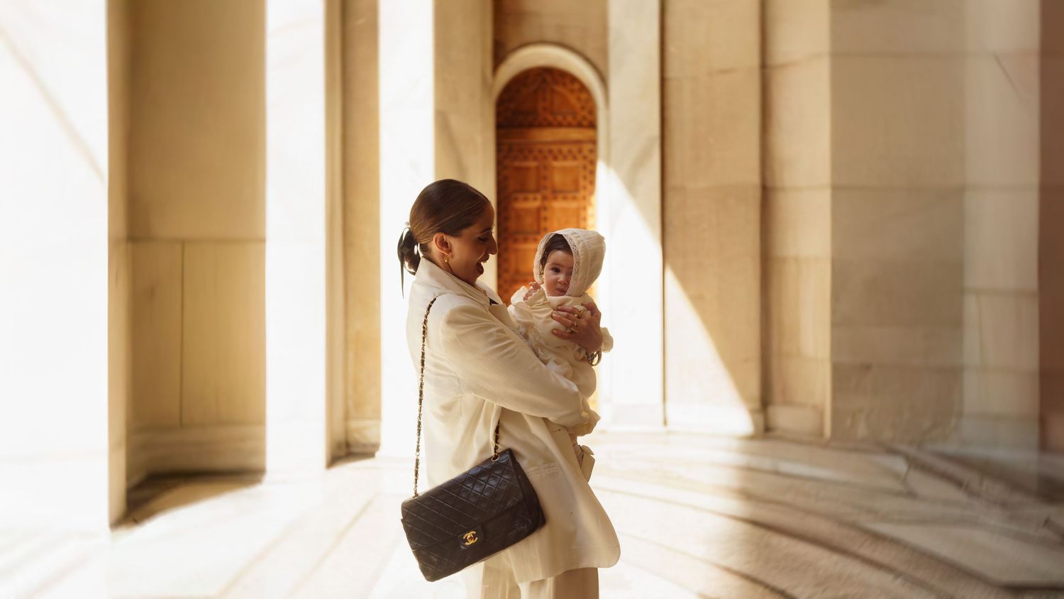 Parent and child sharing tender moment in sunlit colonnade.