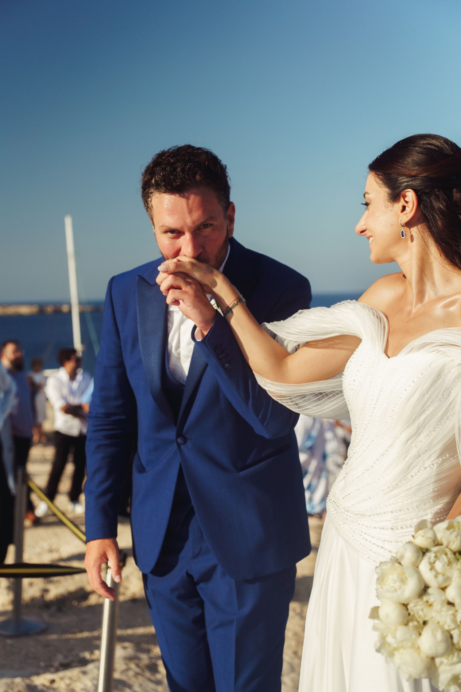 A couple shares a joyful moment during their beach wedding ceremony, with the bride in white and groom in navy blue.