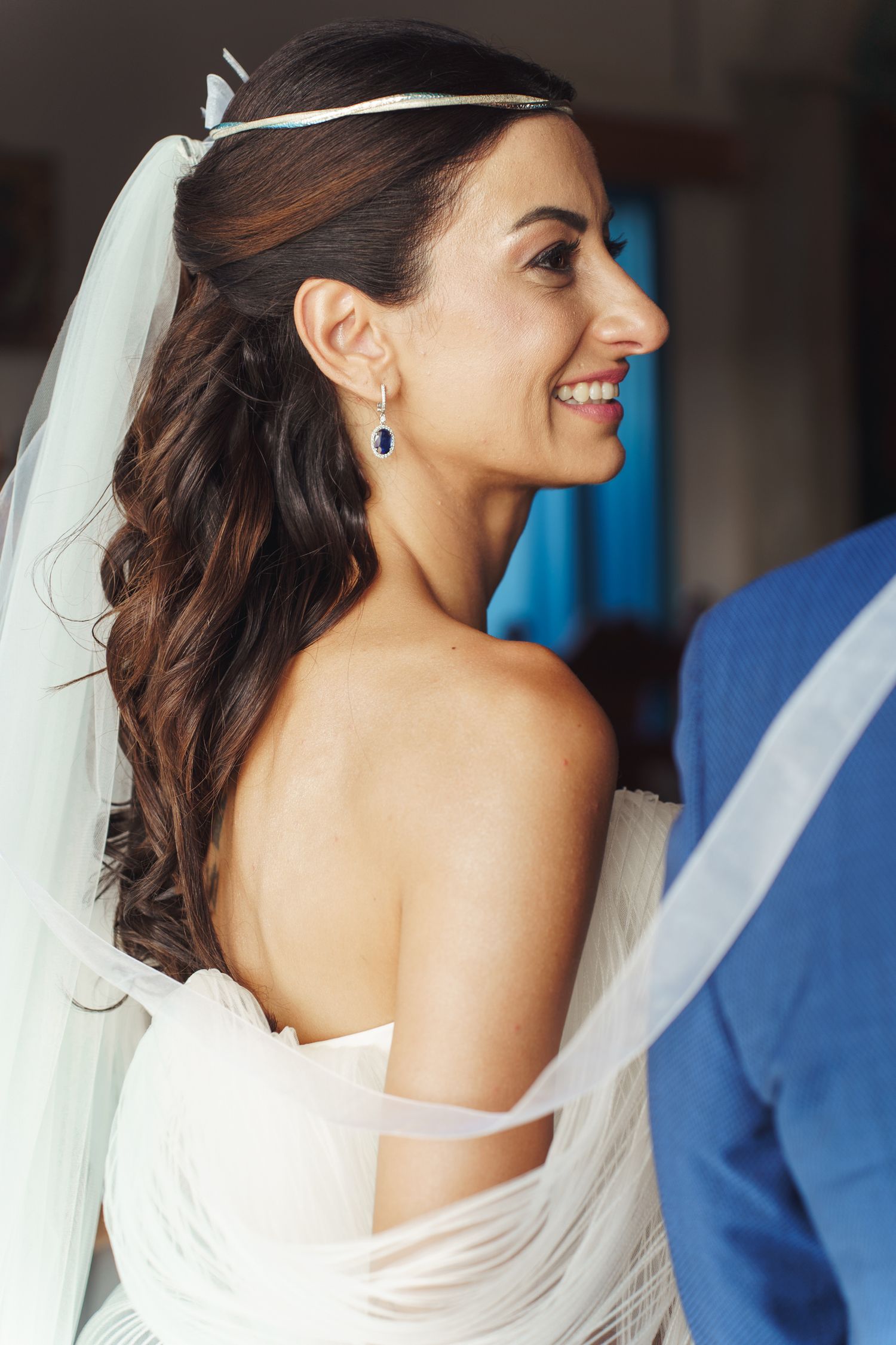 A bride wearing a strapless white gown and long veil smiles while looking to the side.
