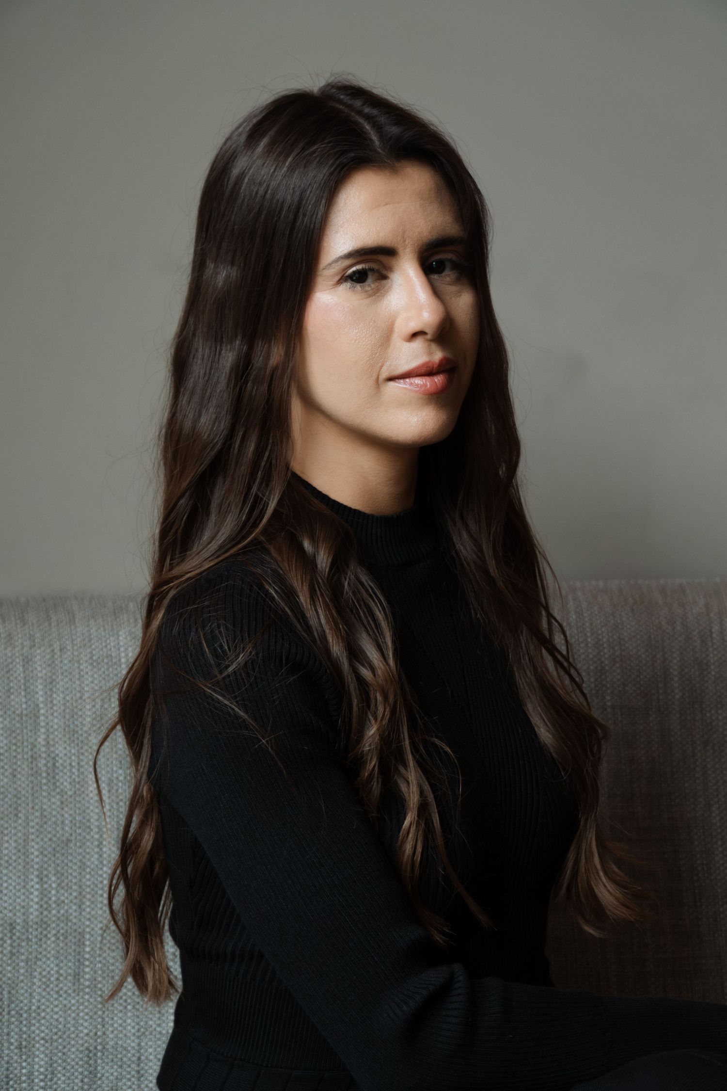 Studio portrait of woman in black sweater with long dark hair against grey background.