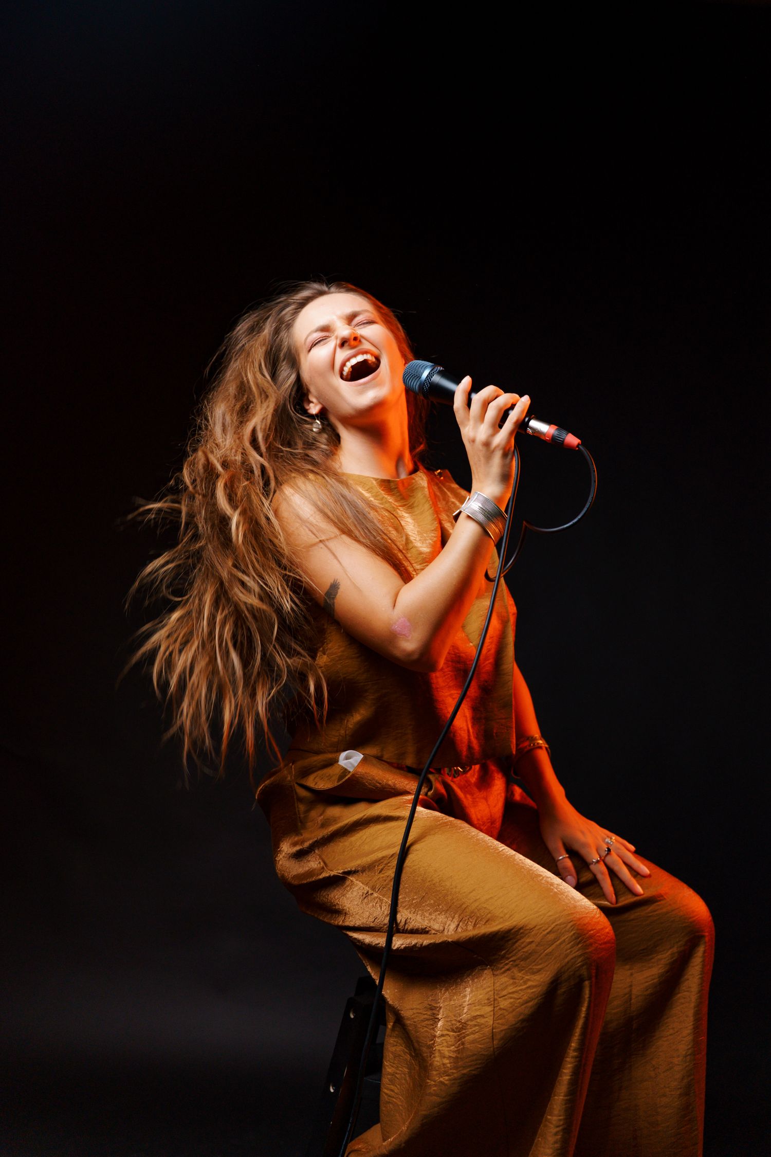 Singer performing passionately on stage with flowing hair and brown outfit in dramatic lighting.