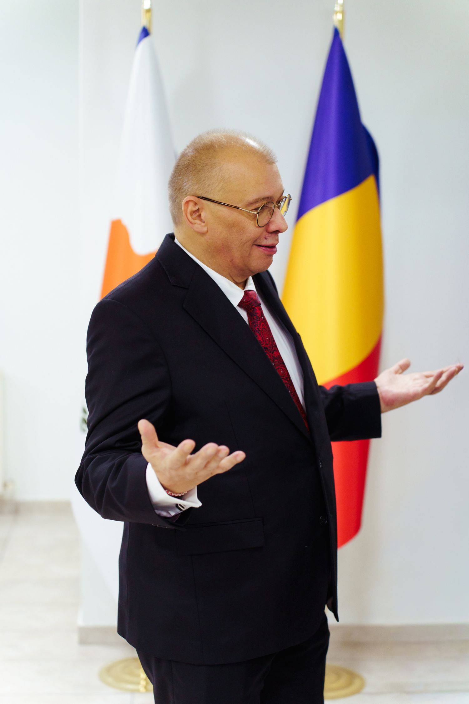 A person in a black suit gestures animatedly in a sequence of four photos against a light background with flags.
