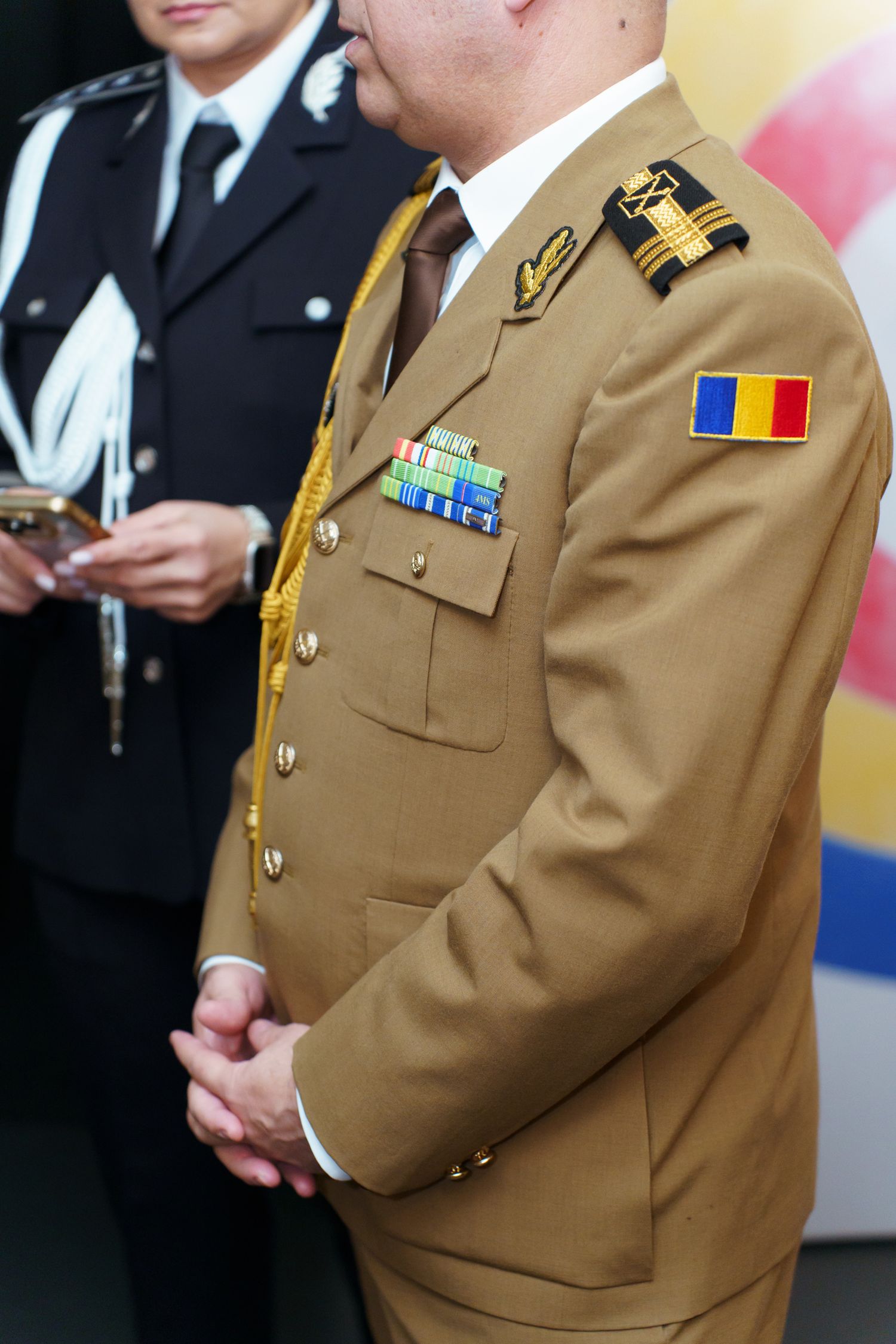 Military personnel in brown dress uniforms with medals and insignia stand in formation at an official ceremony.