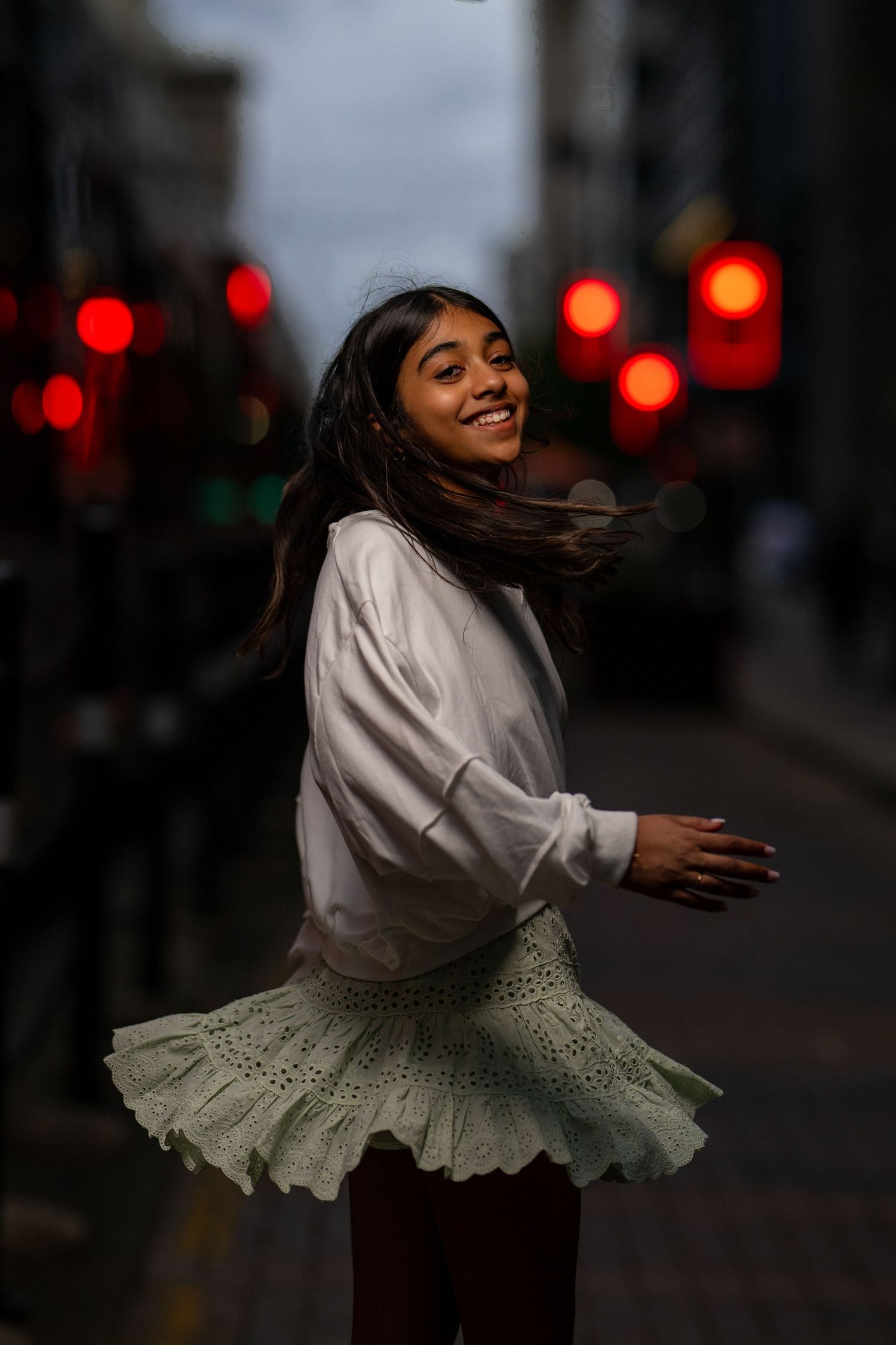 Young woman in white blouse and green skirt twirling joyfully on a city street at night.