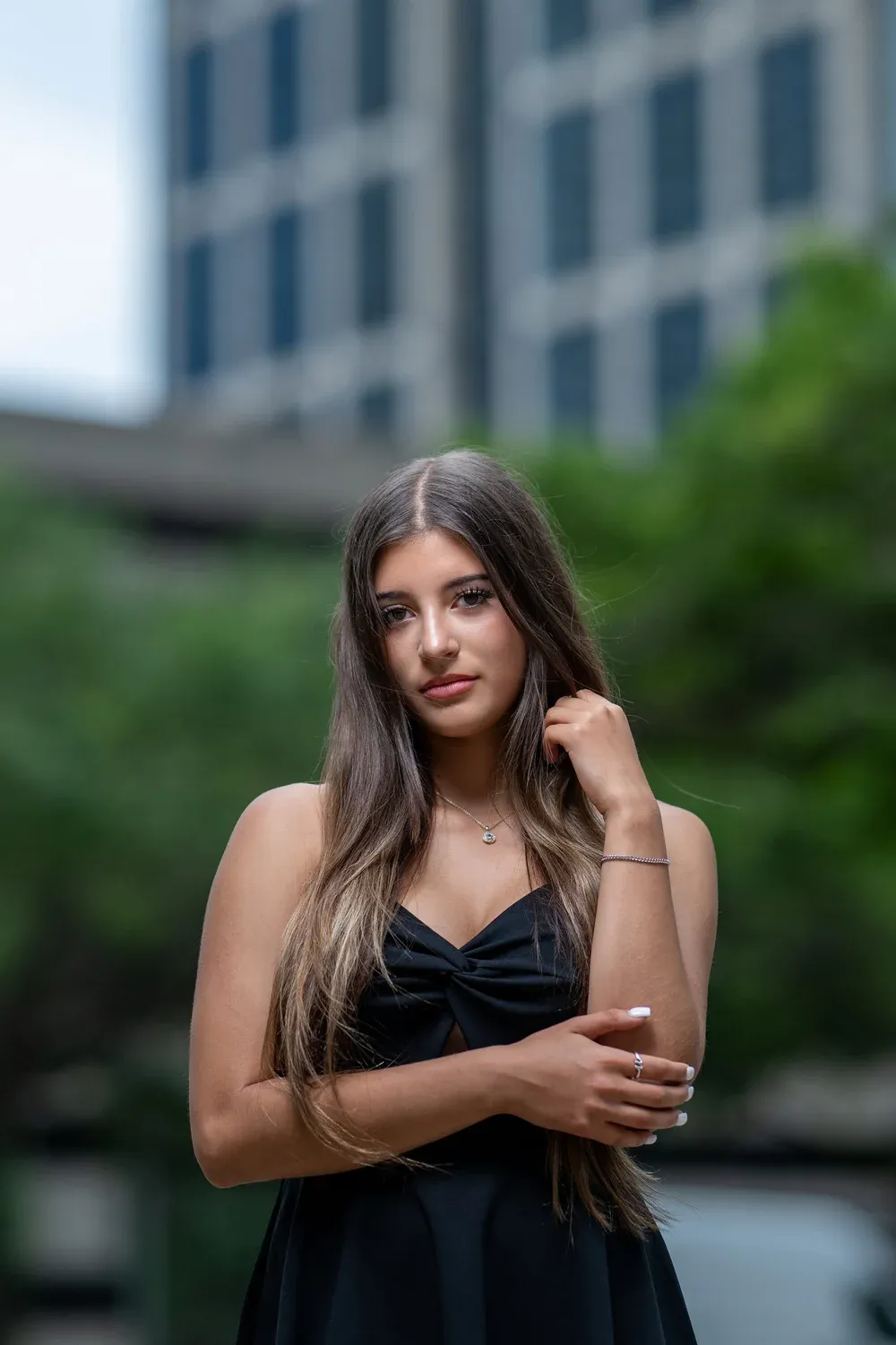 Brunette woman in a black strapless dress standing outdoors in an urban setting.