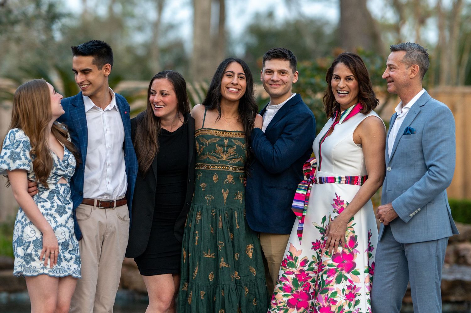 A joyful group of seven people posing together outdoors in elegant attire at a formal gathering.